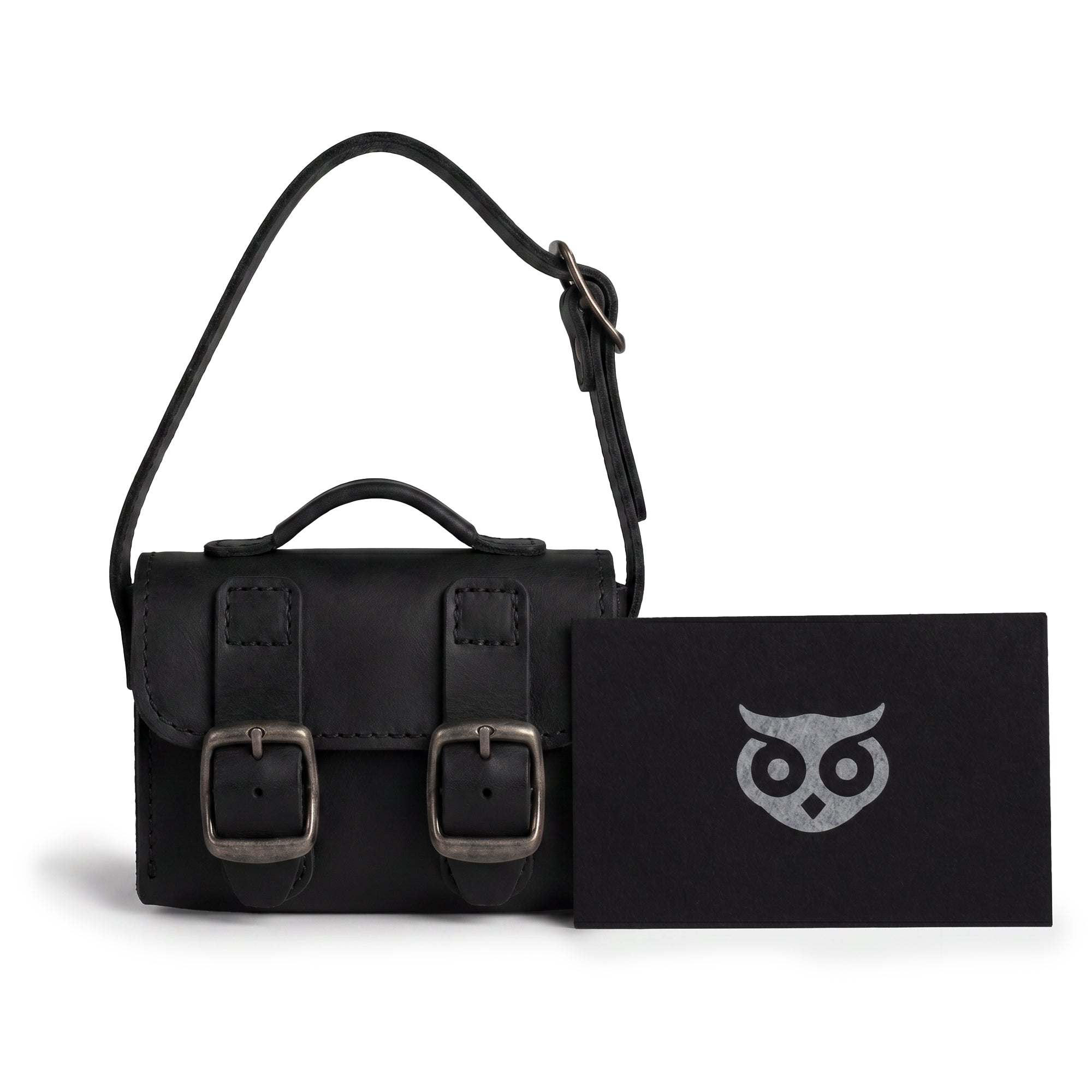 The Black Tiny Messenger Bag by Hide & Drink, featured with accompanying tags. This Mini Messenger Bag Charm, crafted from quality Full Grain Leather, serves as an elegant keychain or handbag accessory. Artisan-made in La Antigua Guatemala, reflecting small batch craftsmanship.
