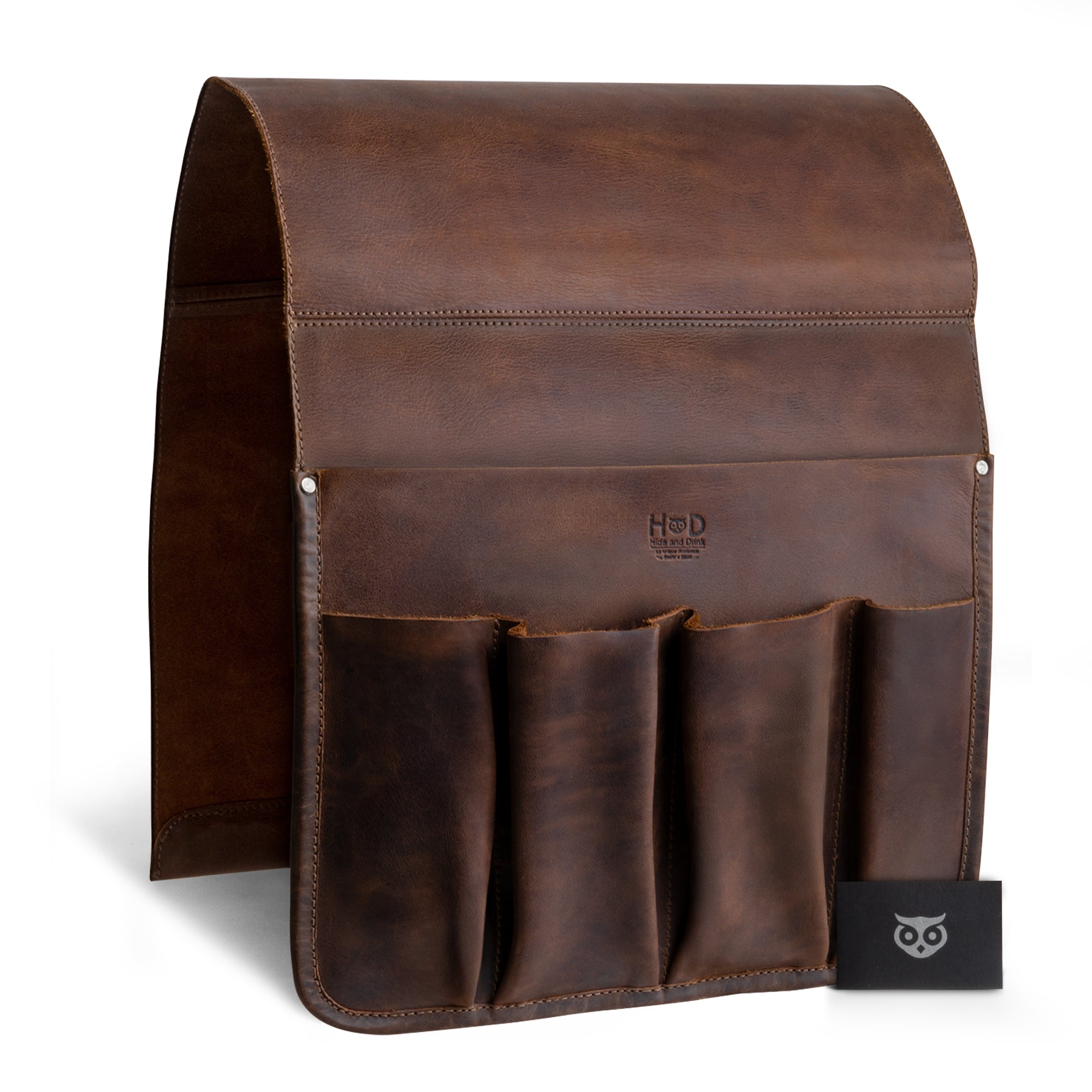Hide & Drink Remote Control Holder showcasing its rich, dark leather and stylish pockets for remotes and magazines. This artistic piece exemplifies handmade craftsmanship from La Antigua Guatemala, emphasizing its role as a sophisticated sofa armrest organizer pouch.
