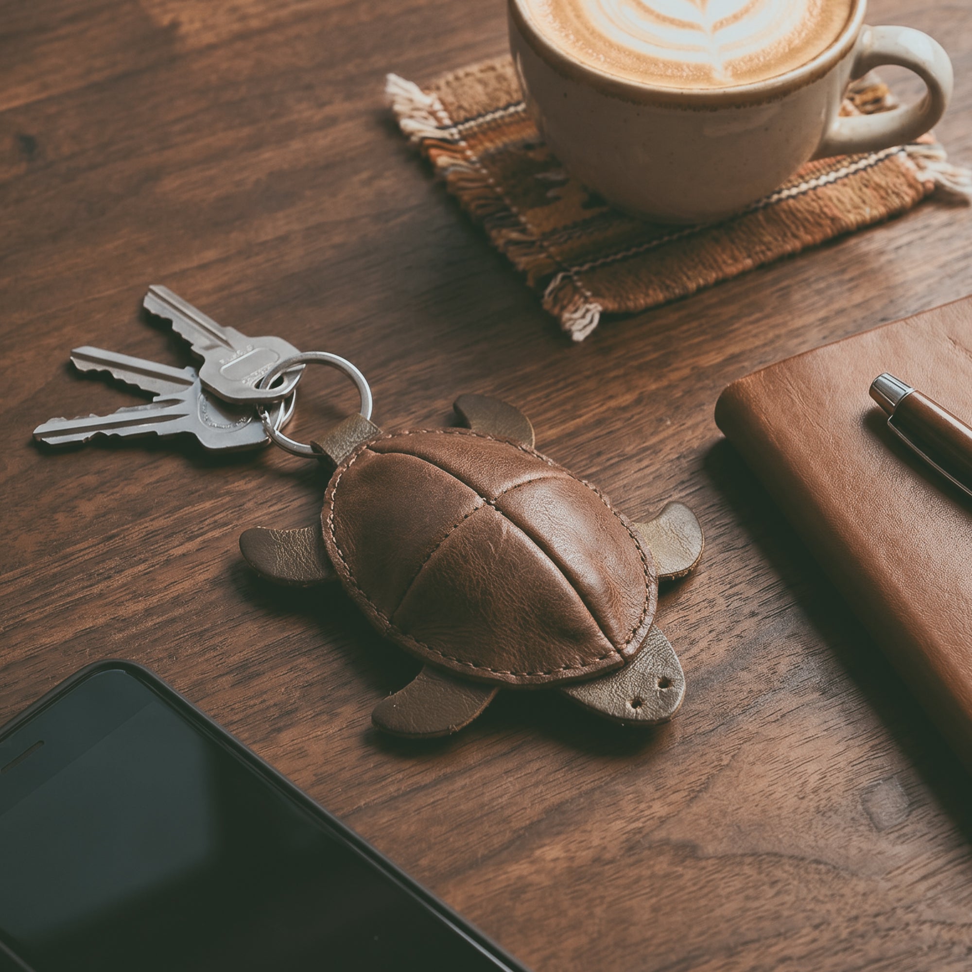 Turtle Mini Pouch Keychain by Hide & Drink, displayed on a wooden desk with keys and a notebook. This Leather Turtle Coin Purse or change pouch is made from Full Grain Leather, demonstrating unique artisan craftsmanship from La Antigua Guatemala, perfect for everyday use.