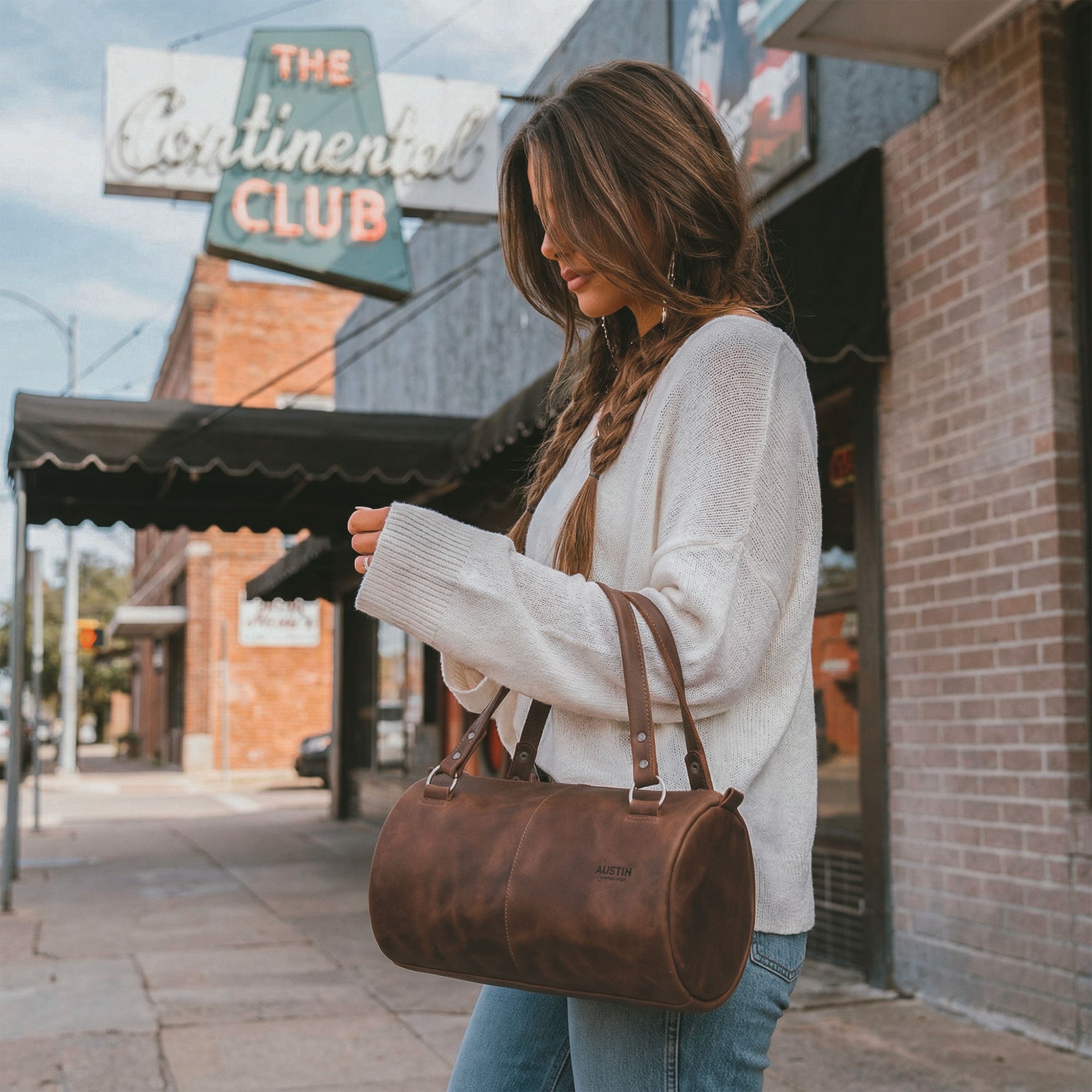 A stylish individual carrying The Rosedale Mini Duffle Bag Handbag by Austin Genuine, demonstrating its chic versatility. Made with full grain leather that is hand cut, hand sewn, and fire branded, this handbag showcases the beauty of artisan small batch production from La Antigua Guatemala & Oaxaca Mexico.