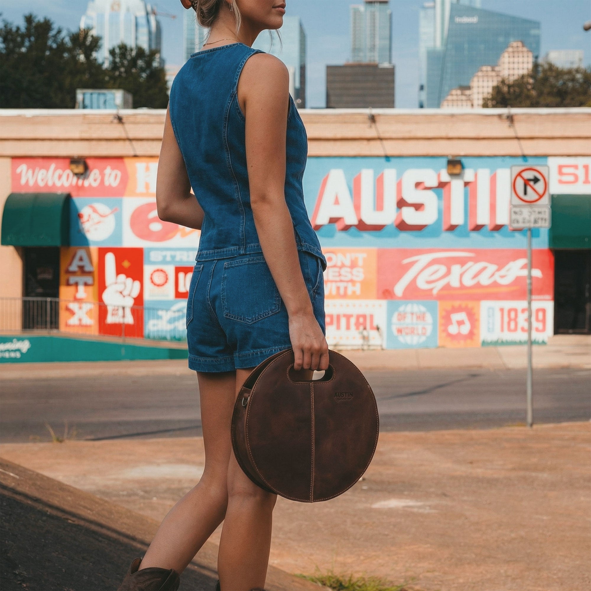 The Pecan Shoulder Bag by Austin Genuine, carried stylishly in an urban setting, highlighting its round shape and full grain leather material, emphasizing small batch production techniques, hand cut, hand sewn, and artisan craftsmanship, made in La Antigua Guatemala & Oaxaca Mexico.