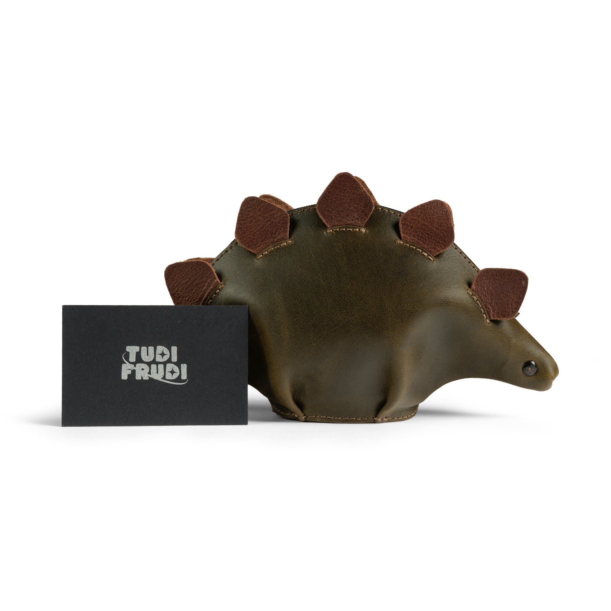 The Leather Dinosaur Stegosaurus Pouch by Tudi Frudi is displayed alongside a branded card, emphasizing its artisan quality. This playful zippered change purse combines fashion and function, highlighting small batch production techniques from La Antigua Guatemala and Oaxaca Mexico, perfect for both men and women.