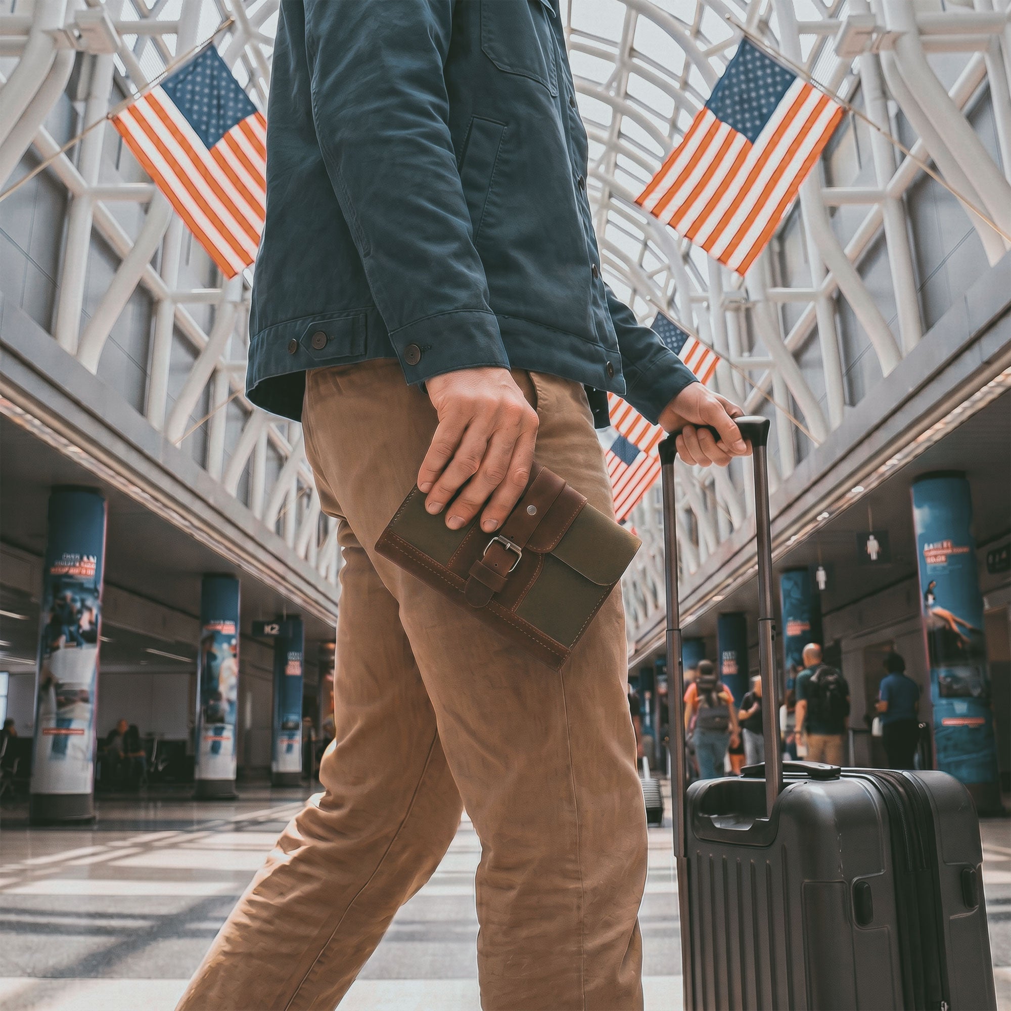 A traveler holding the Vintage Adventure Passport Cover by Littlefield Chicago in an airport. This stylish passport cover serves as an Adventure Passport Holder for Travel, made of durable Full Grain Leather with a convenient wallet organizer design. Each piece is handcrafted in small batches by artisans in La Antigua Guatemala & Oaxaca Mexico.