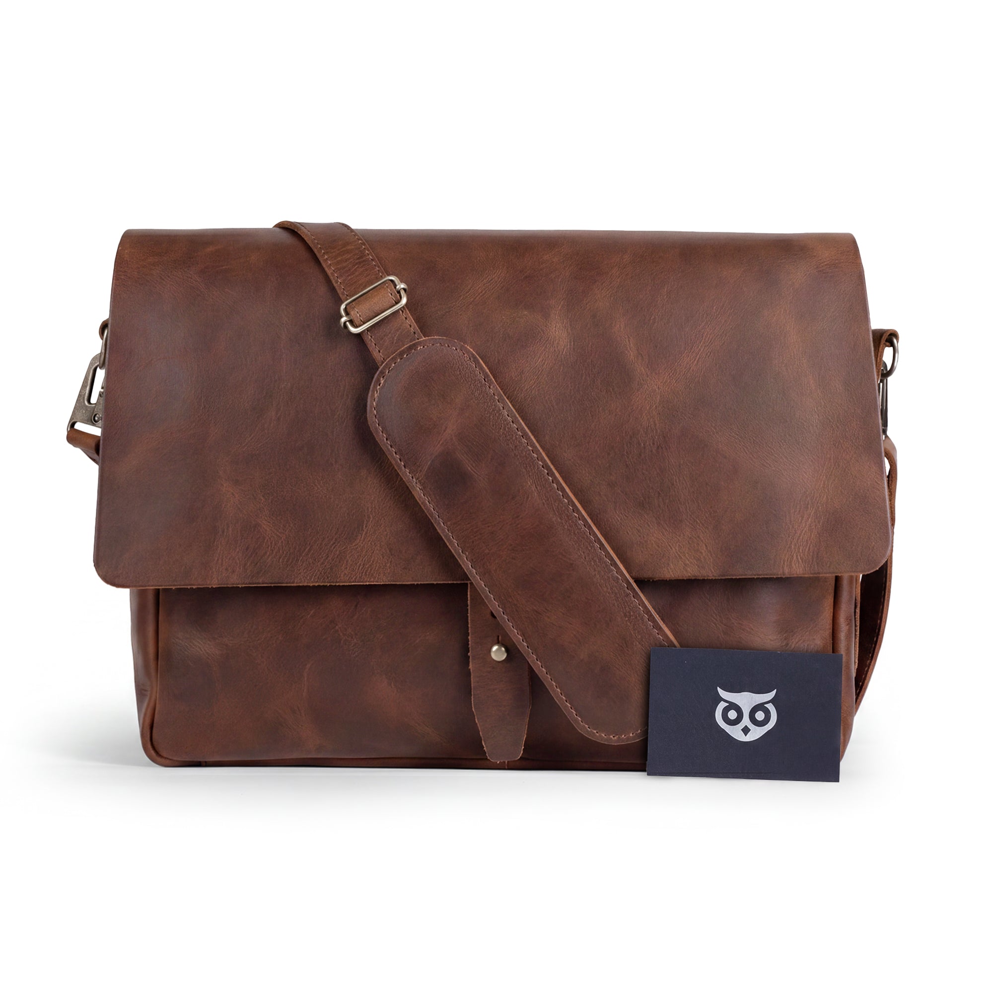 Close-up of Hide & Drink's Messenger Bag with Adjustable Strap, displaying leather tags and the quality of materials used. This travel accessory offers 13-14 inch laptop storage and features a classic portfolio design, embodying small batch production and artisan handmade craftsmanship. Handmade in La Antigua Guatemala & Oaxaca Mexico.