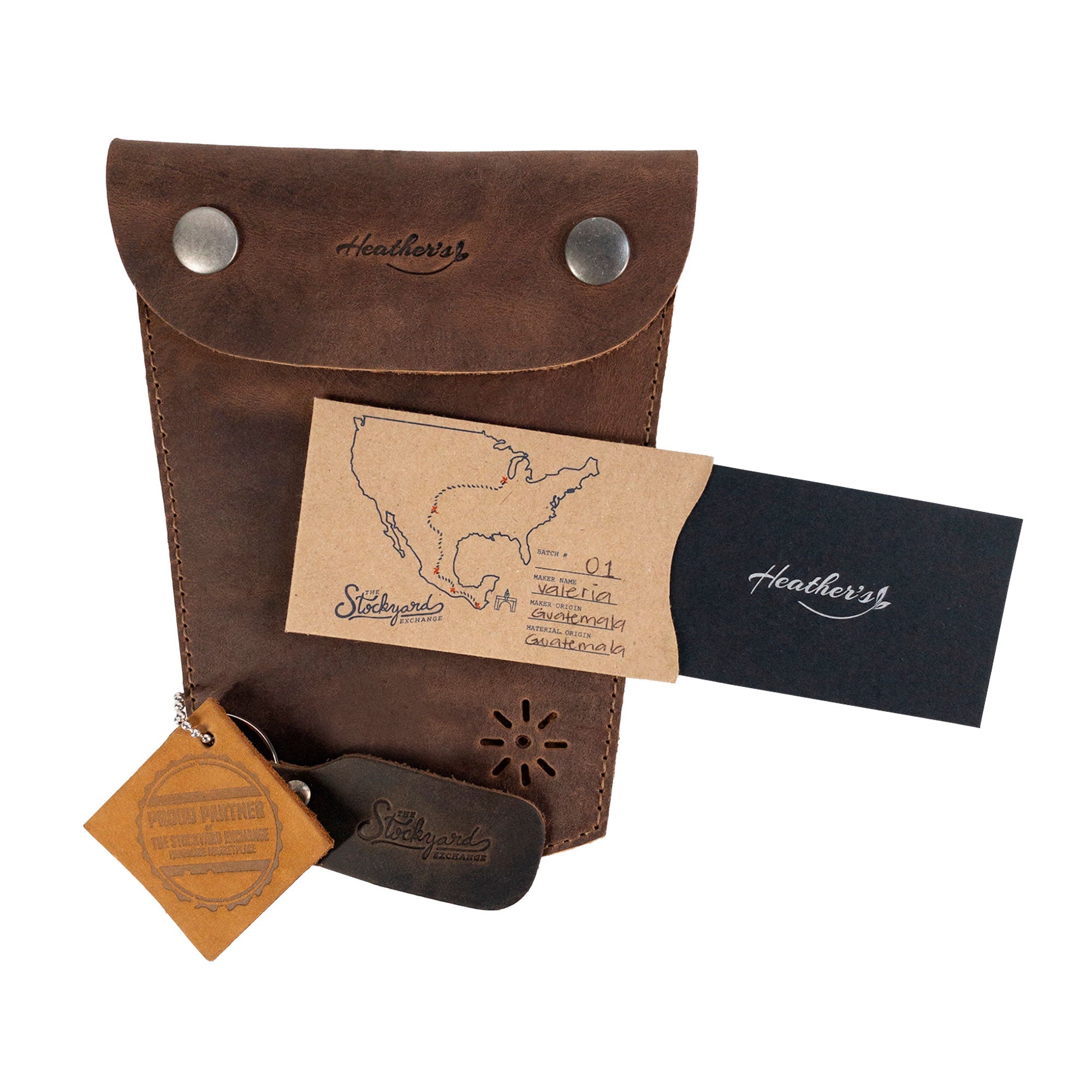 Heather's Essential Mini Bag alongside artisan cards and tags, highlighting its handmade heritage. This mini bag for women functions as an essential case for glasses, makeup, USB, cables, and cash, making it a thoughtful travel accessory. Each piece is made from full grain leather in La Antigua Guatemala, showcasing small batch production methods and artisan craftsmanship.