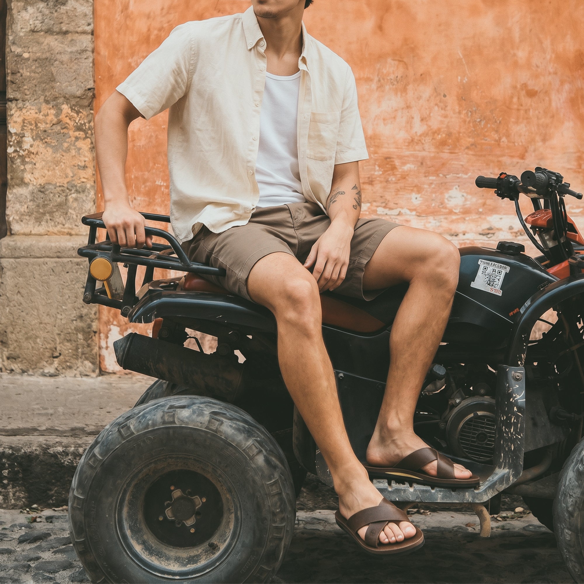 A casual setting with a person wearing The Wanderer Arch Comfort Sandals while sitting on an ATV. Made by La Leche, these sandals offer both comfort and style, suitable for various activities. Crafted from Full Grain Leather and Memory Foam, each pair is handmade and showcases fine artisan skills, perfect for outdoor adventures.
