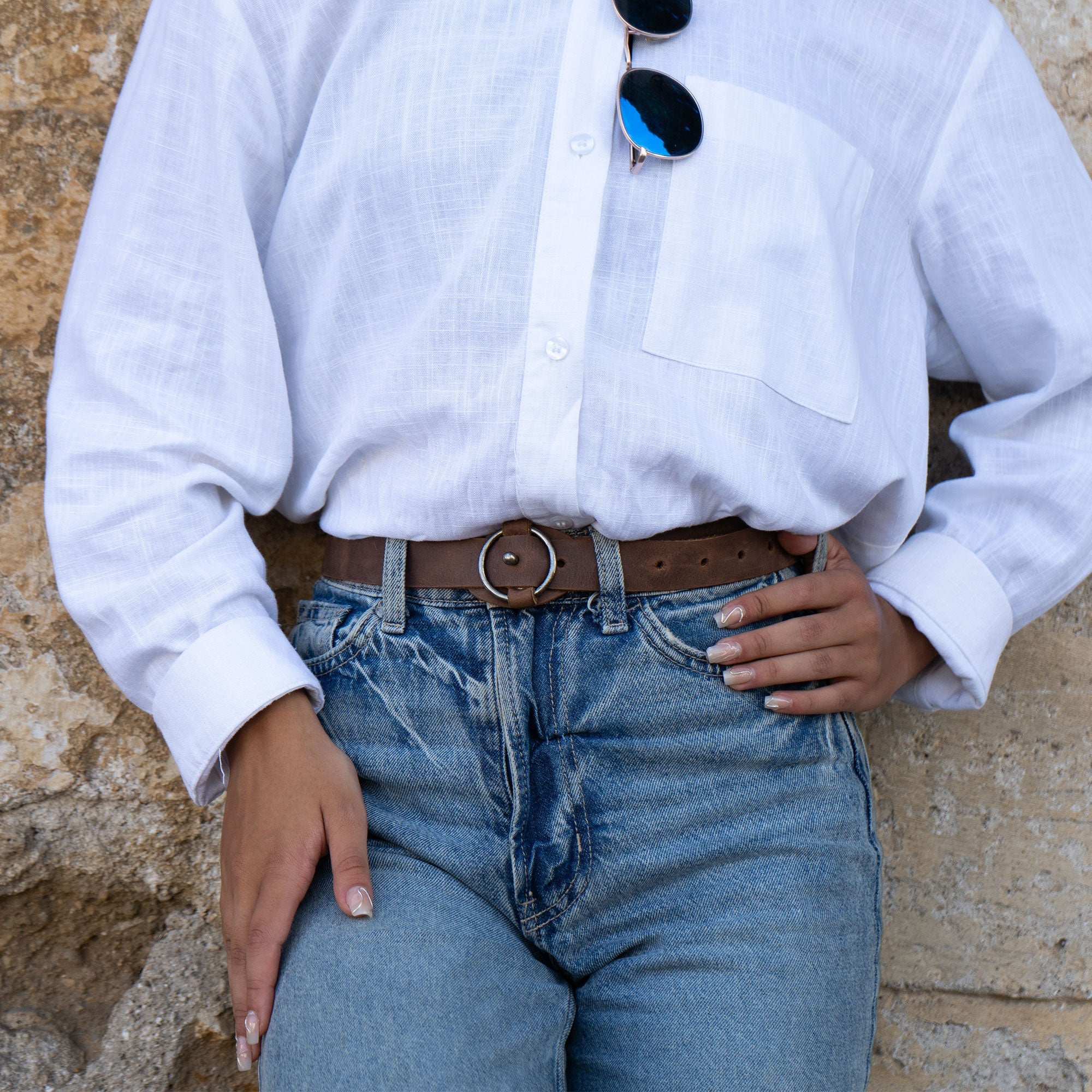 Model wearing Heather's Belt for Women with Ring Closure with a classic white shirt and jeans. This full grain leather belt adds elegance as a waist strap, illustrating its versatility as a no-buckle belt and stylish belly accessory, handmade by artisans.