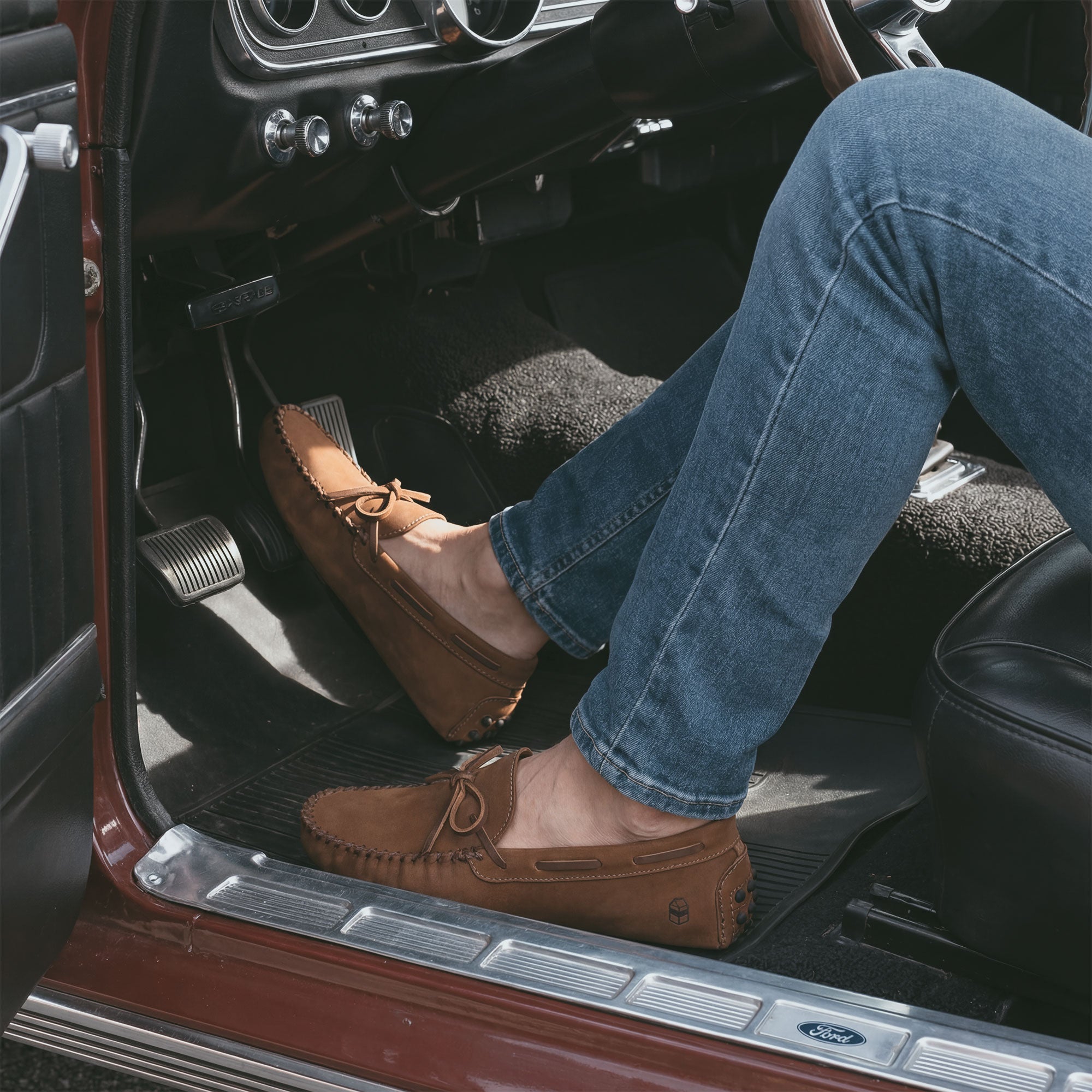 A close-up of a person wearing The Roadster Leather Driving Moccasins inside a classic car, showcasing their Full Grain Leather craftsmanship. These artisan shoes from La Leche are handmade in La Antigua Guatemala & Oaxaca Mexico.