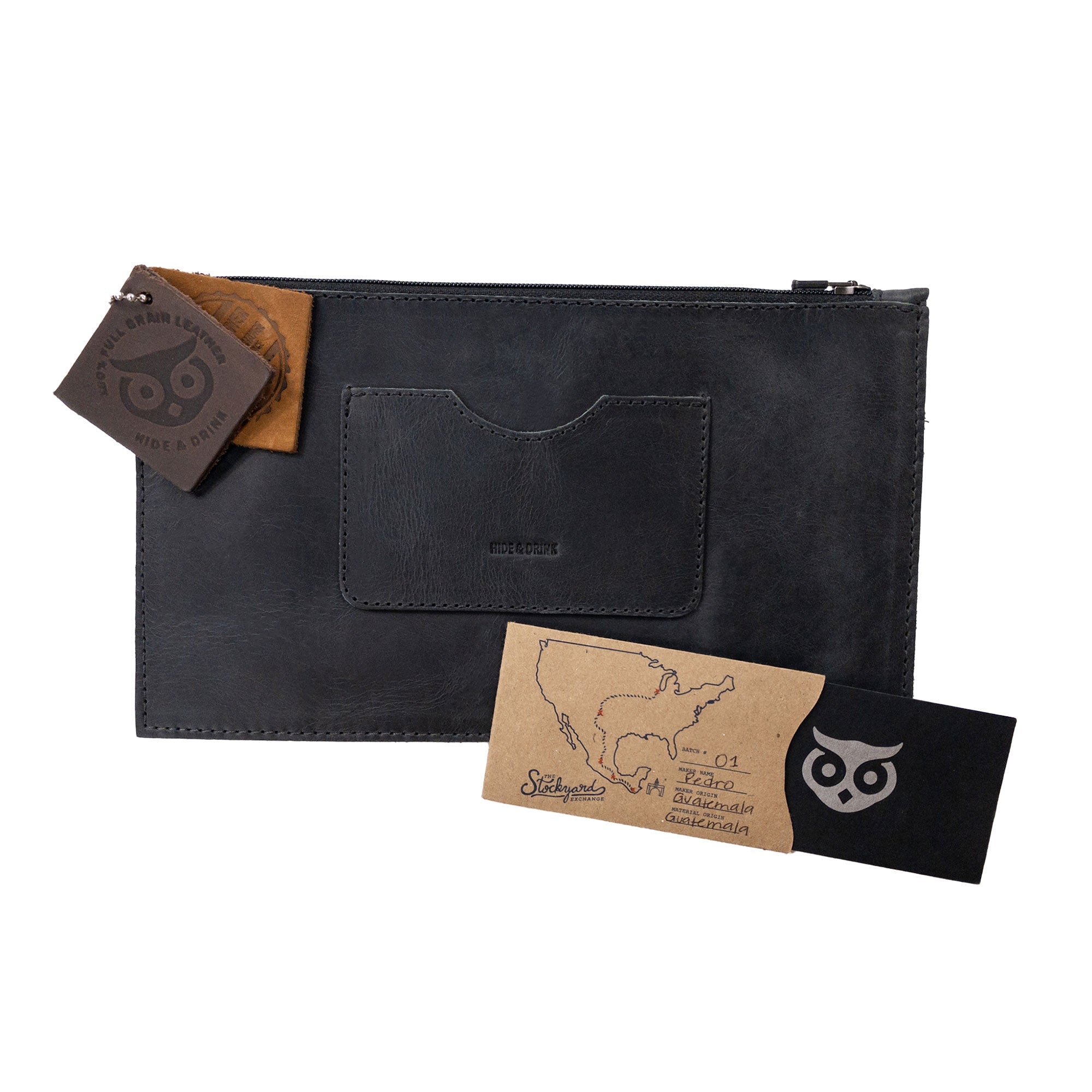 A black rectangular zippered handbag by Hide & Drink accompanied by leather care tags, designed for women emphasizing quality. This full grain leather female purse includes a card slot, highlighting artisan craftsmanship through small batch production and handmade techniques in La Antigua Guatemala & Oaxaca Mexico.