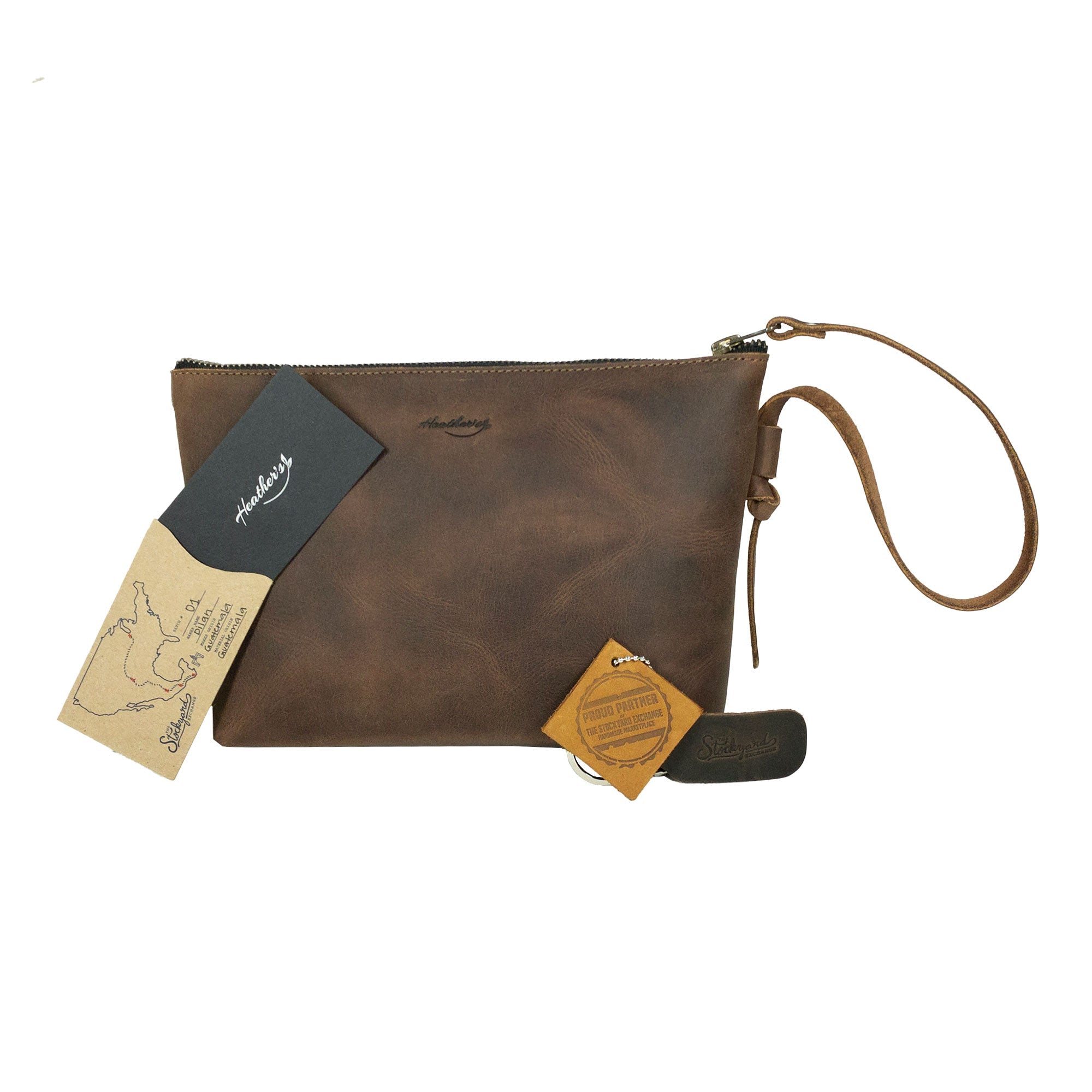 Heather's Clutch Bag with Strap, displayed with care labels and original tags, showcasing its artisan origin. This stylish Full Grain Leather clutch is a practical wrist wallet for cards and money, ideal for makeup and cosmetic storage, handmade in La Antigua Guatemala & Oaxaca Mexico.