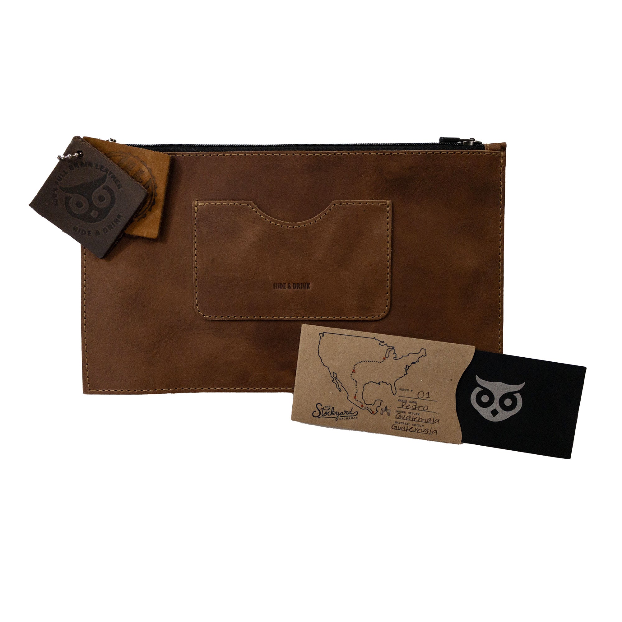 A brown rectangular zippered handbag by Hide & Drink accompanied by leather care tags, perfect for women, showcasing its card slot. This full grain leather purse demonstrates artisan craftsmanship and the quality of small batch production techniques in La Antigua Guatemala & Oaxaca Mexico.