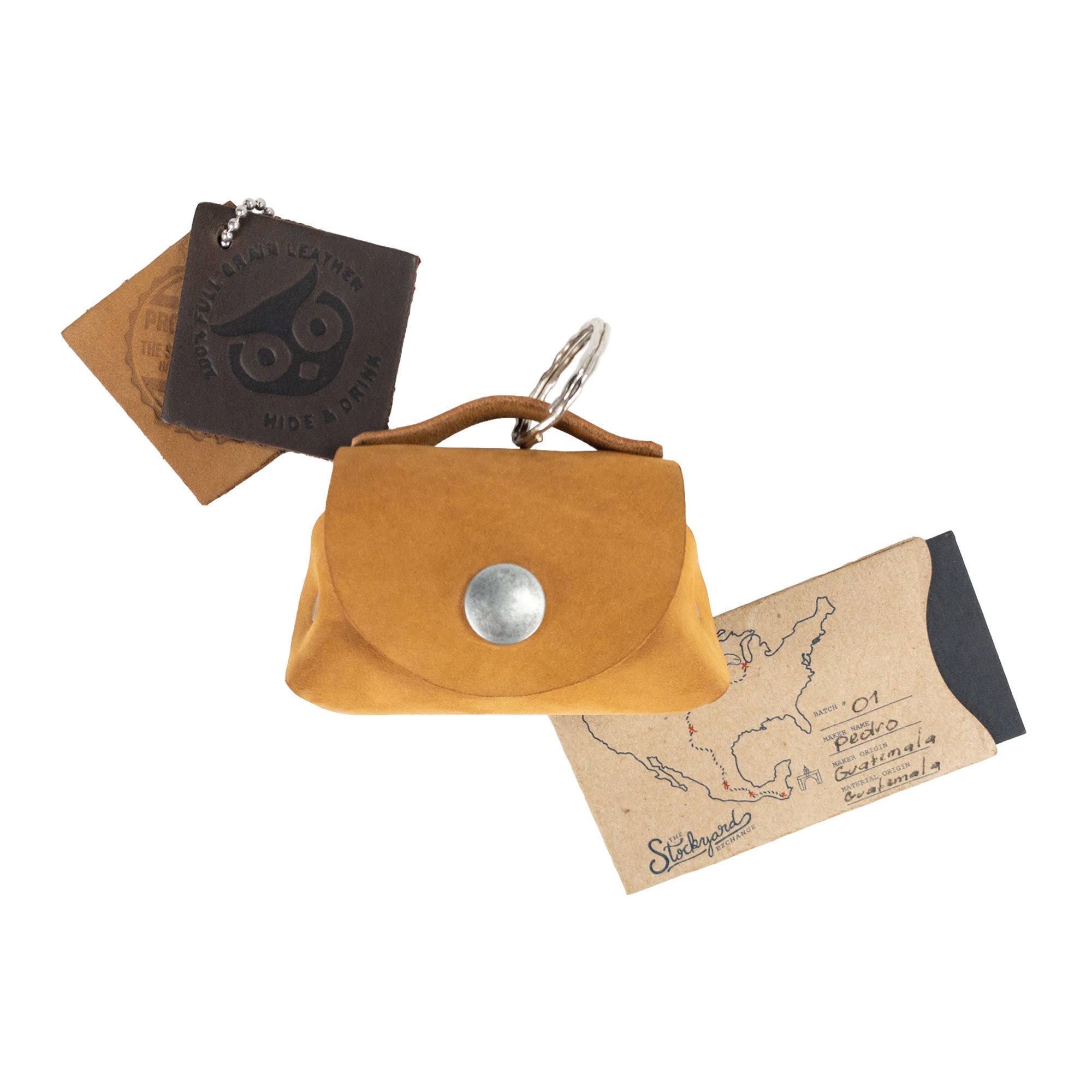 Top view of the mustard Tiny Handbag Keychain by Hide & Drink alongside its unique packaging, showcasing the Tiny Handbag with Key Ring Holder crafted from Full Grain Leather. This artisan product emphasizes Small Batch Production, and is Hand Cut, Hand Sewn, and Fire Branded, highlighting its Handmade craftsmanship from La Antigua Guatemala & Oaxaca Mexico.
