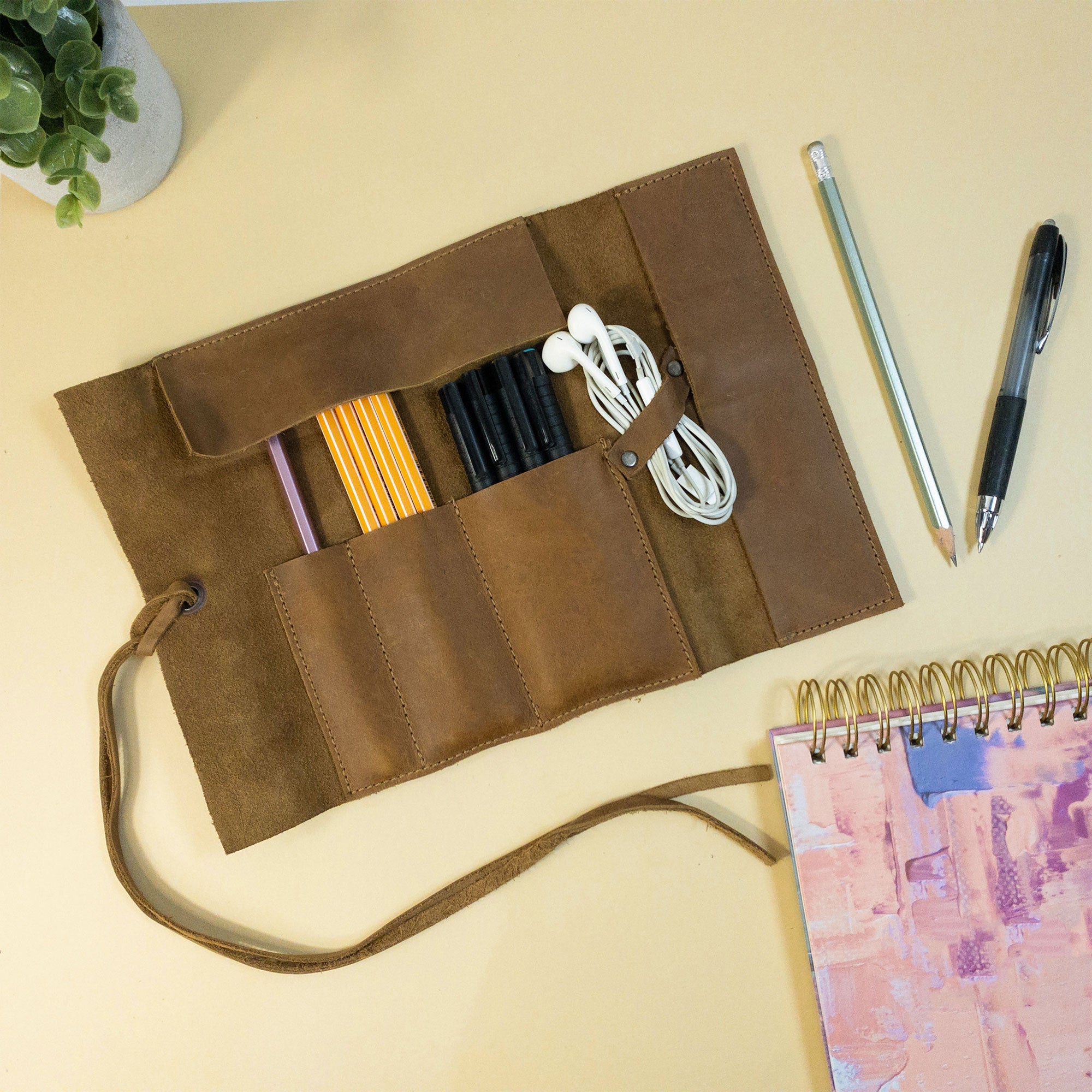 Hide & Drink Multi Purpose Pencil Roll presented open, emphasizing its versatility for different tools. This rustic, handmade organizer showcases quality craftsmanship in full grain leather, perfect for art supplies and work necessities.