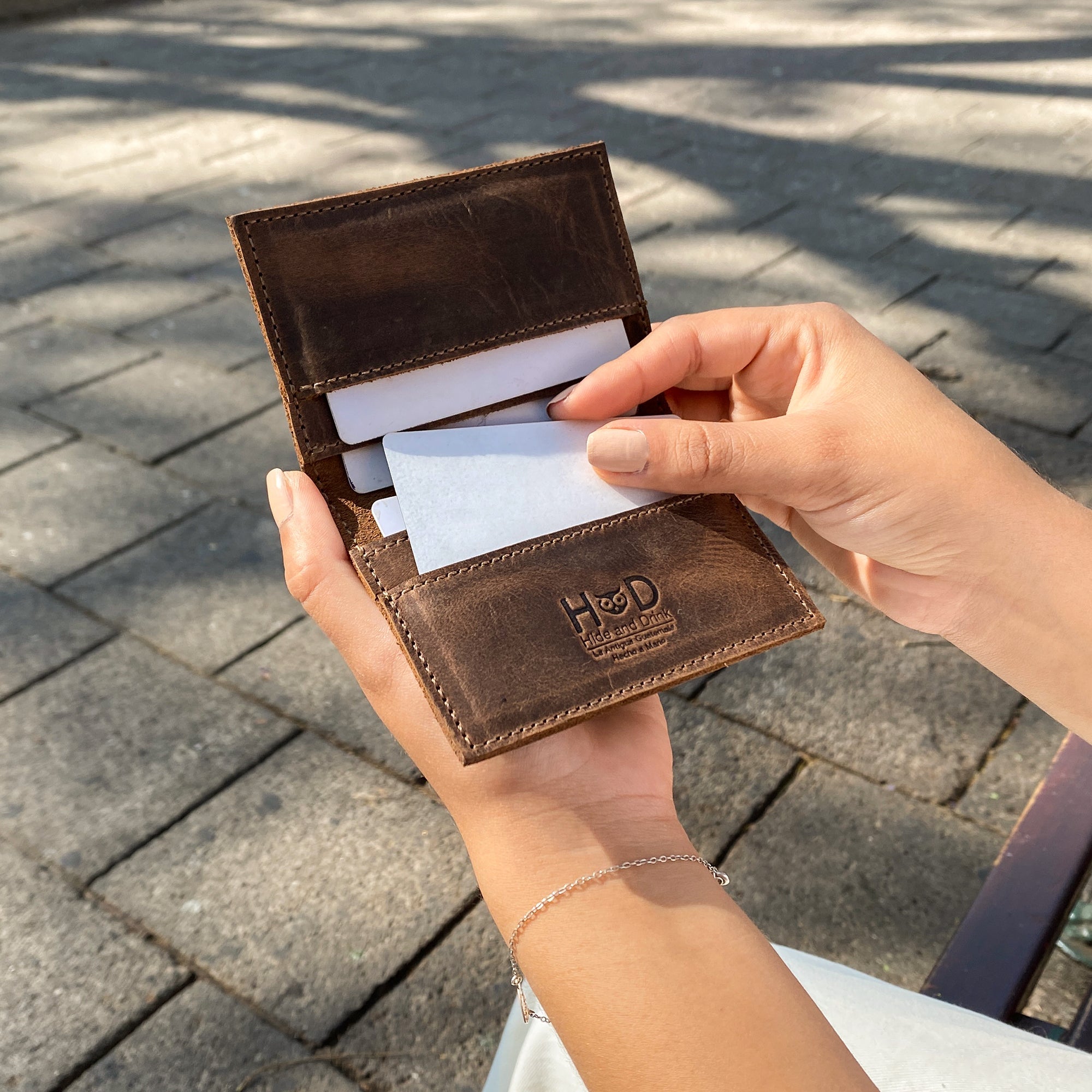 Bifold Horizontal Card Wallet by Hide & Drink being held, demonstrating its practical use as a minimalist traveller wallet, designed as an organizer to hold up to 8 cards, made from high-quality full grain leather, showcasing small batch production, hand cut, hand sewn, fire branded artistry, handmade in La Antigua Guatemala & Oaxaca Mexico.