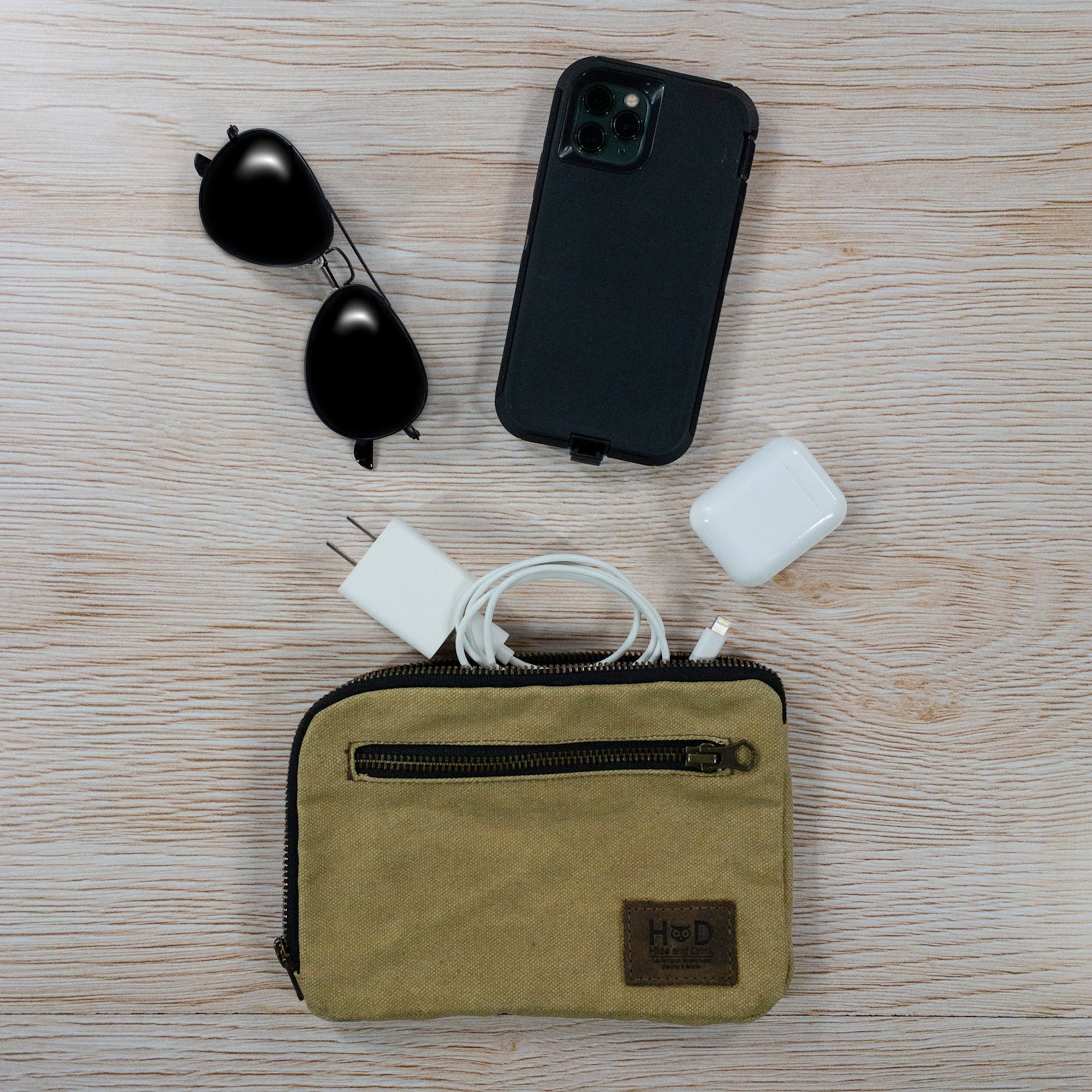 Hide & Drink's Zipper Gear Pouch next to sunglasses and electronic items, demonstrating its utility as a travel accessory, made from water resistant waxed canvas.