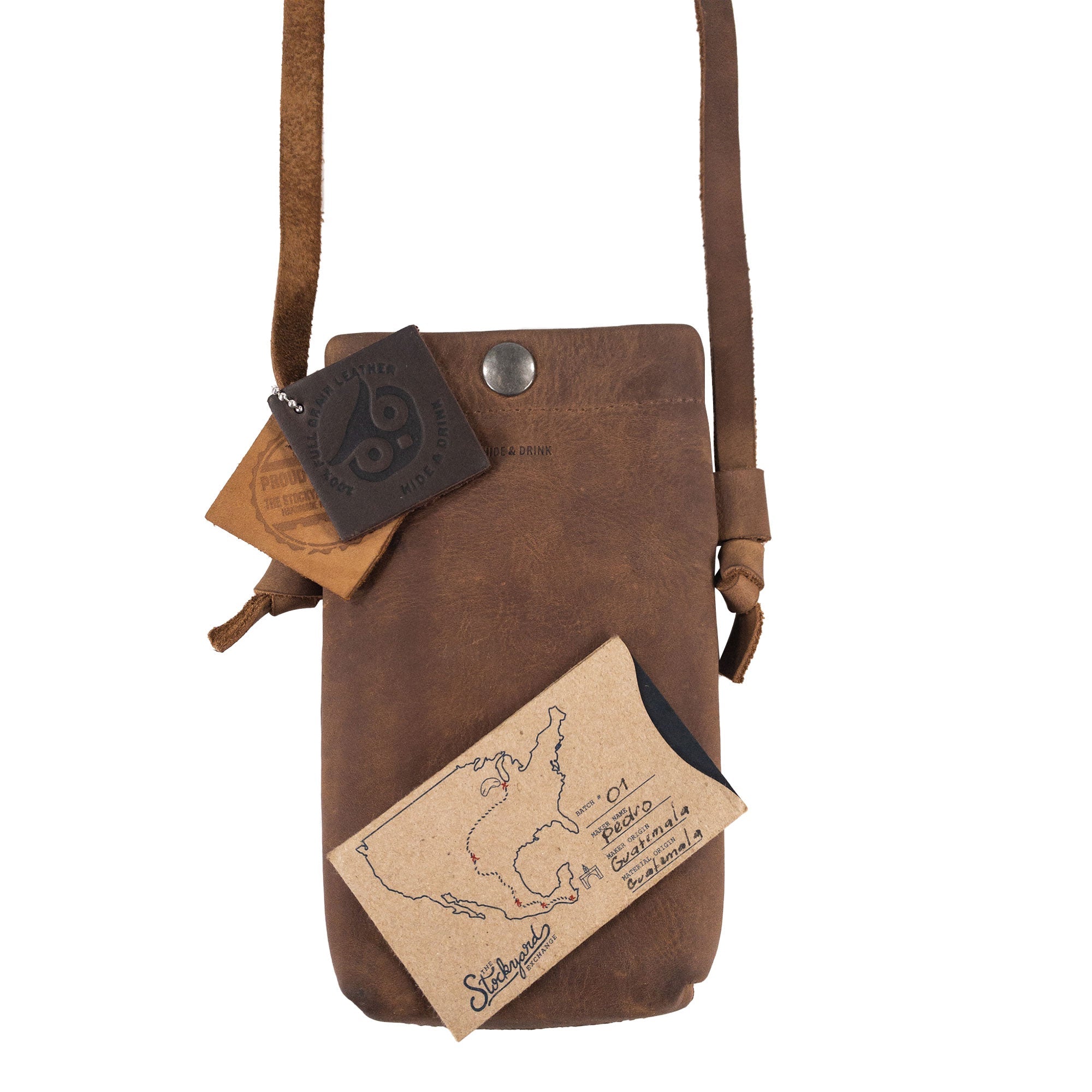 Close-up of the Hide & Drink Cell Phone Shoulder Bag alongside branded leather tags, emphasizing its handcrafted quality. This full grain leather phone bag is a practical and stylish choice for those looking for a shoulder or crossbody bag for cellphone carrying, proudly made in La Antigua Guatemala & Oaxaca Mexico.