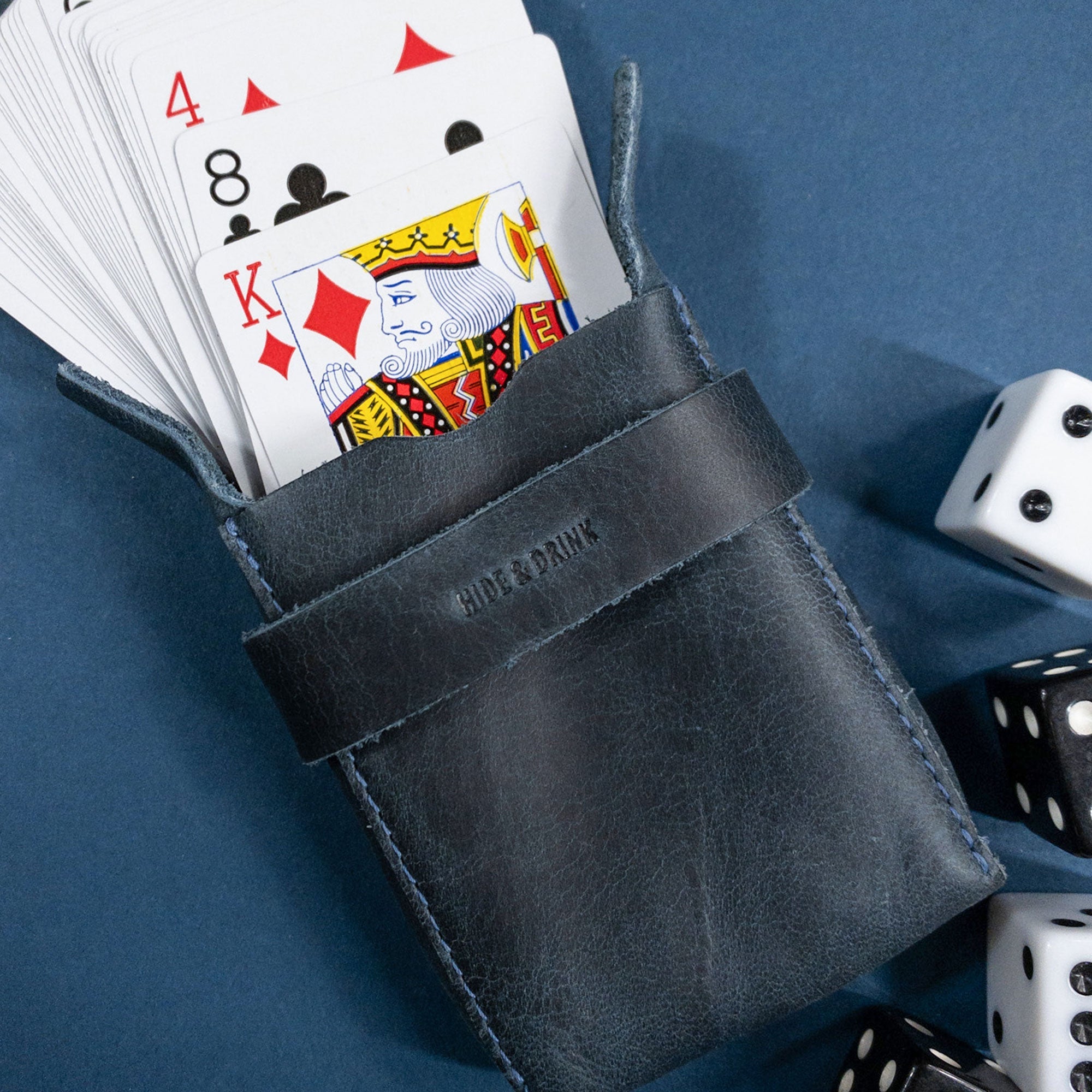 Hide & Drink's navy Playing Card Case displayed with an Ace of spades card. This classic case for playing cards (not included) is a stylish travel accessory featuring secure storage in durable full grain leather. Artisan-crafted in La Antigua Guatemala, it showcases talented craftsmanship from StockyardX.