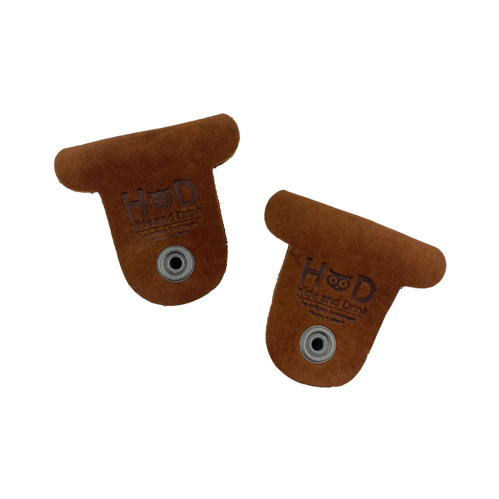 Two brown Dog Shaped Cord Keepers featured with Hide & Drink branding, made from premium Full Grain Leather for stylish cord management. Dog Shaped Cord Keeper (Cord Clam) 2-Pack, Full Grain Leather, StockyardX, Small Batch Production, Hand Cut, Hand Sewn, Fire Branded, Artisan, Handmade in La Antigua Guatemala & Oaxaca Mexico.