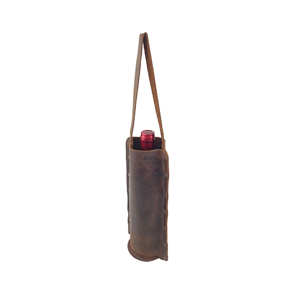 Rustic Wine Carrier For Standard 750ml Bordeaux Bottle by Hide & Drink, displayed with a 750ml Bordeaux bottle inside. This Single Wine Carrier made from Full Grain Leather showcases small batch production methods, hand cutting, and hand sewing, with fire branding, handcrafted in La Antigua Guatemala & Oaxaca Mexico.