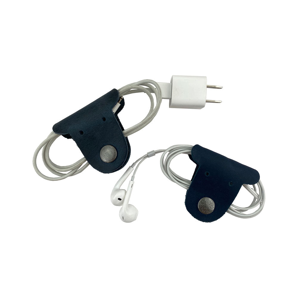 Two navy blue Dog Shaped Cord Keepers organizing earbuds and charging cords, a cute and functional design by Hide & Drink. Dog Shaped Cord Keeper (Cord Clam) 2-Pack, Full Grain Leather, StockyardX, Small Batch Production, Hand Cut, Hand Sewn, Fire Branded, Artisan, Handmade in La Antigua Guatemala & Oaxaca Mexico.