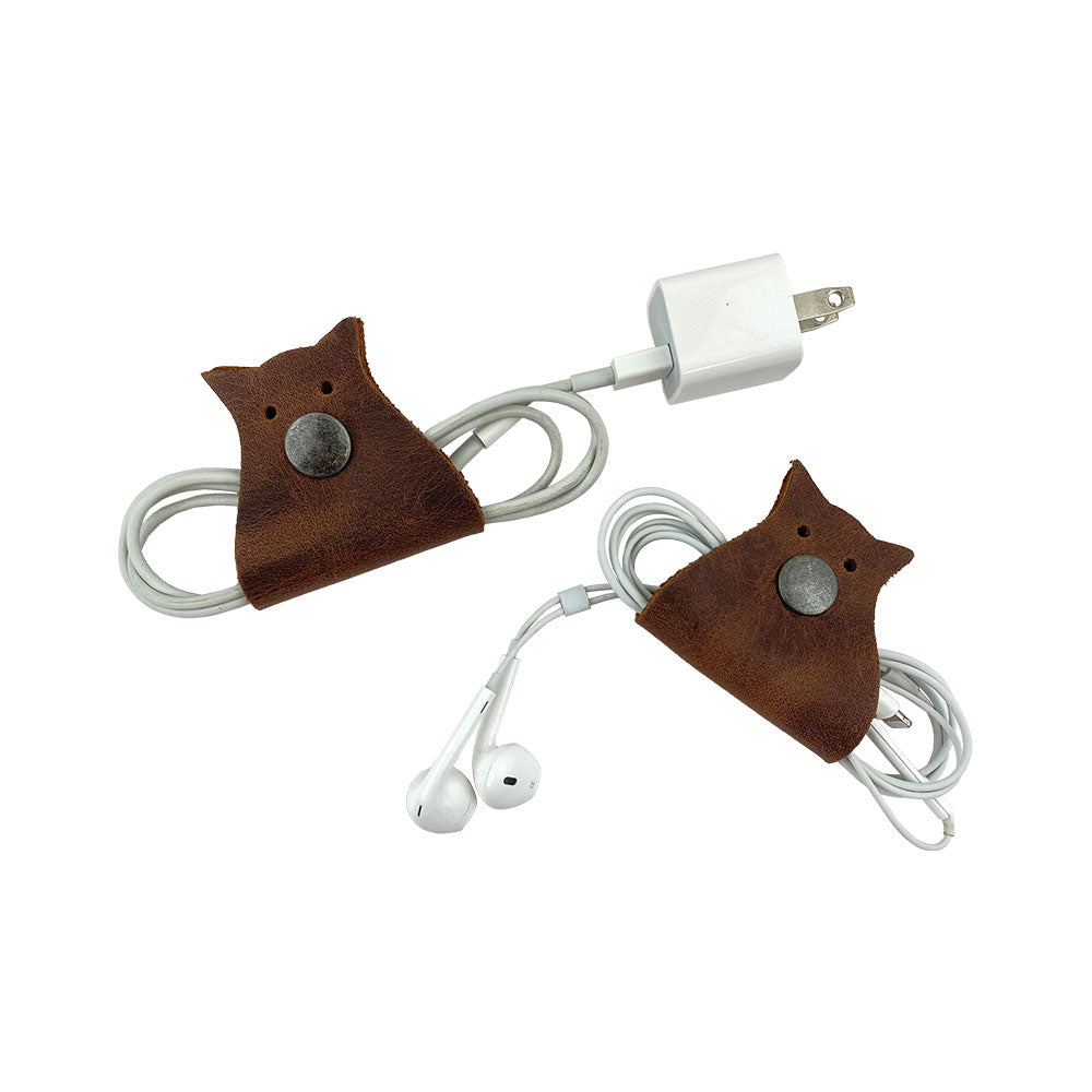Owl Shaped Cord Keeper (2-Pack) by Hide & Drink showcasing two elegantly crafted cord holders in rich brown leather. Owl Shaped Cord Keeper (Cord Clam) 2-Pack. Full Grain Leather, StockyardX, Small Batch Production, Hand Cut, Hand Sewn, Fire Branded, Artisan, Handmade in La Antigua Guatemala & Oaxaca Mexico.