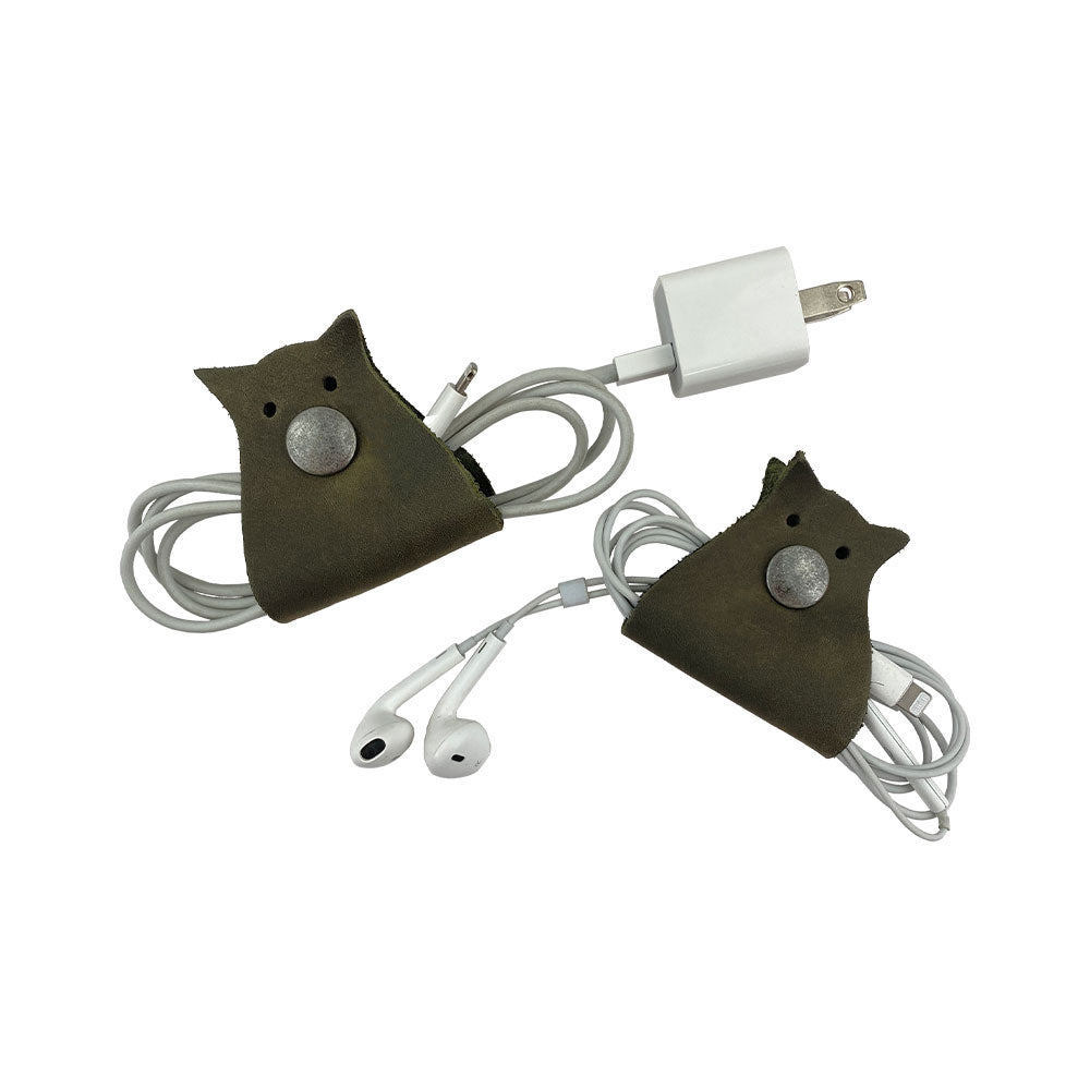 Owl Shaped Cord Keeper (2-Pack) by Hide & Drink paired with earphones, showcasing a neat way to manage cords in style. Owl Shaped Cord Keeper (Cord Clam) 2-Pack. Full Grain Leather, StockyardX, Small Batch Production, Hand Cut, Hand Sewn, Fire Branded, Artisan, Handmade in La Antigua Guatemala & Oaxaca Mexico.