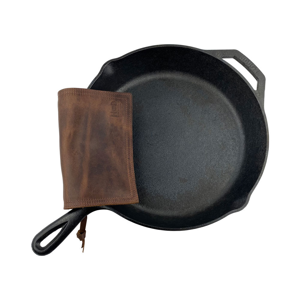 Hide & Drink Pot Pad next to a cast iron skillet in use. This double-layered rustic leather pot pad is perfect for handling hot cookware safely and stylishly.