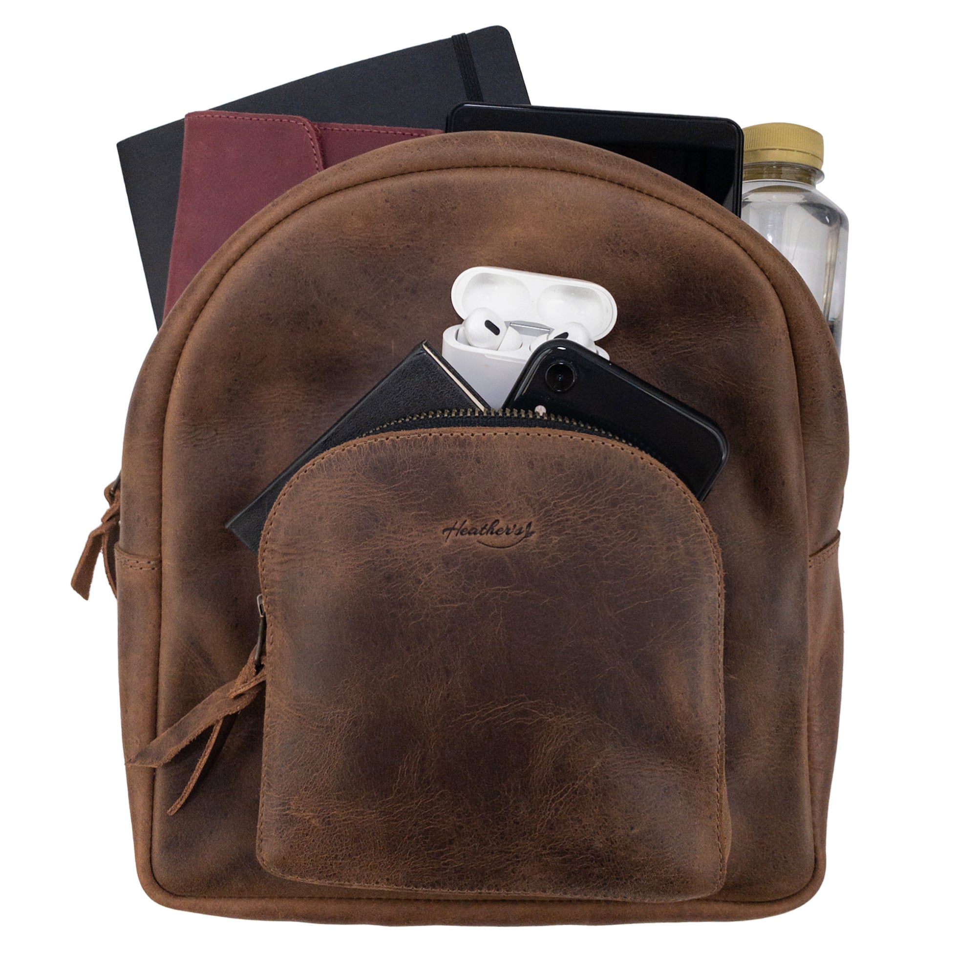 The Heather's Minimalist Backpack packed with essentials such as notebooks, a water bottle, and a phone, illustrating its capacity for organization. Constructed from rich full grain leather and featuring adjustable straps, this artisan-made backpack is perfect for travel. Handmade in La Antigua Guatemala, it highlights small batch production techniques.