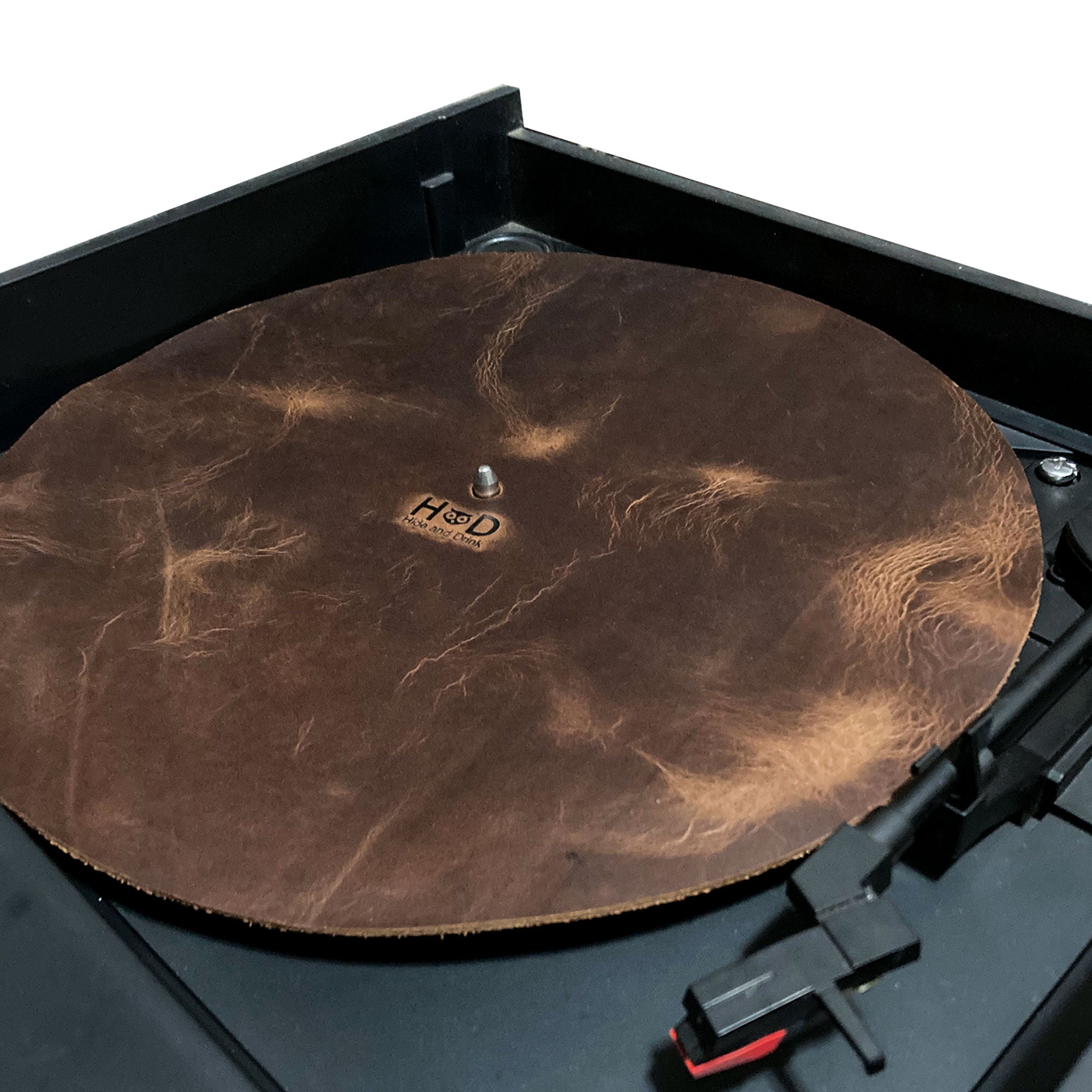 Hide & Drink Turntable Slipmat in place on a turntable, enhancing the vinyl listening experience. This classy, antistatic cover is handmade from premium full grain leather, designed for noise reduction and durability, reflecting the artisan craftsmanship of small batch production.