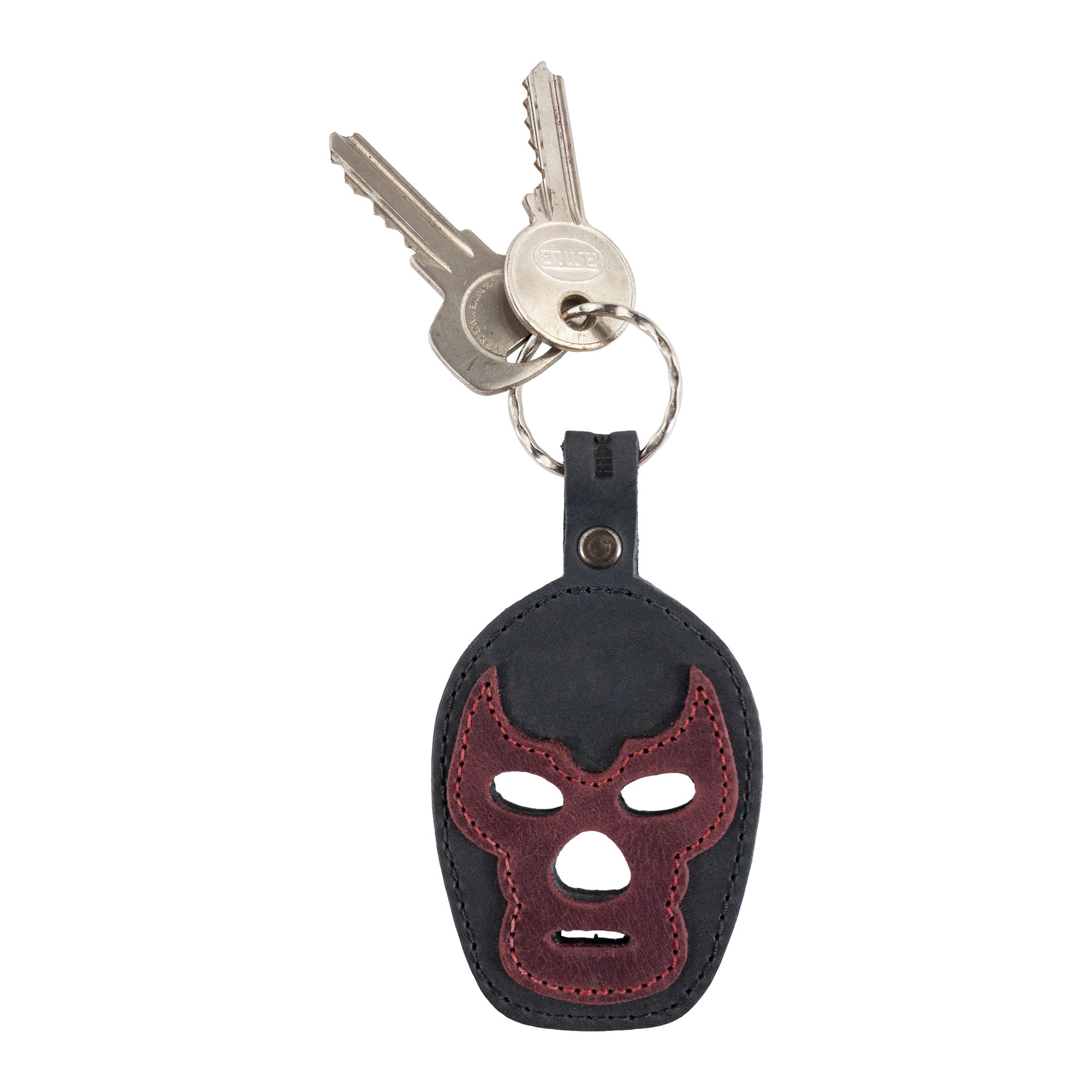 The Luchador Mask Leather Keychain attached to a ring of individual keys, showcasing its utility and design. This keyring from Hide & Drink serves as both a stylish accessory and a practical key organizer. Crafted from full grain leather, it represents small batch production by artisans who hand cut, hand sew, and fire brand each piece in La Antigua Guatemala and Oaxaca Mexico.