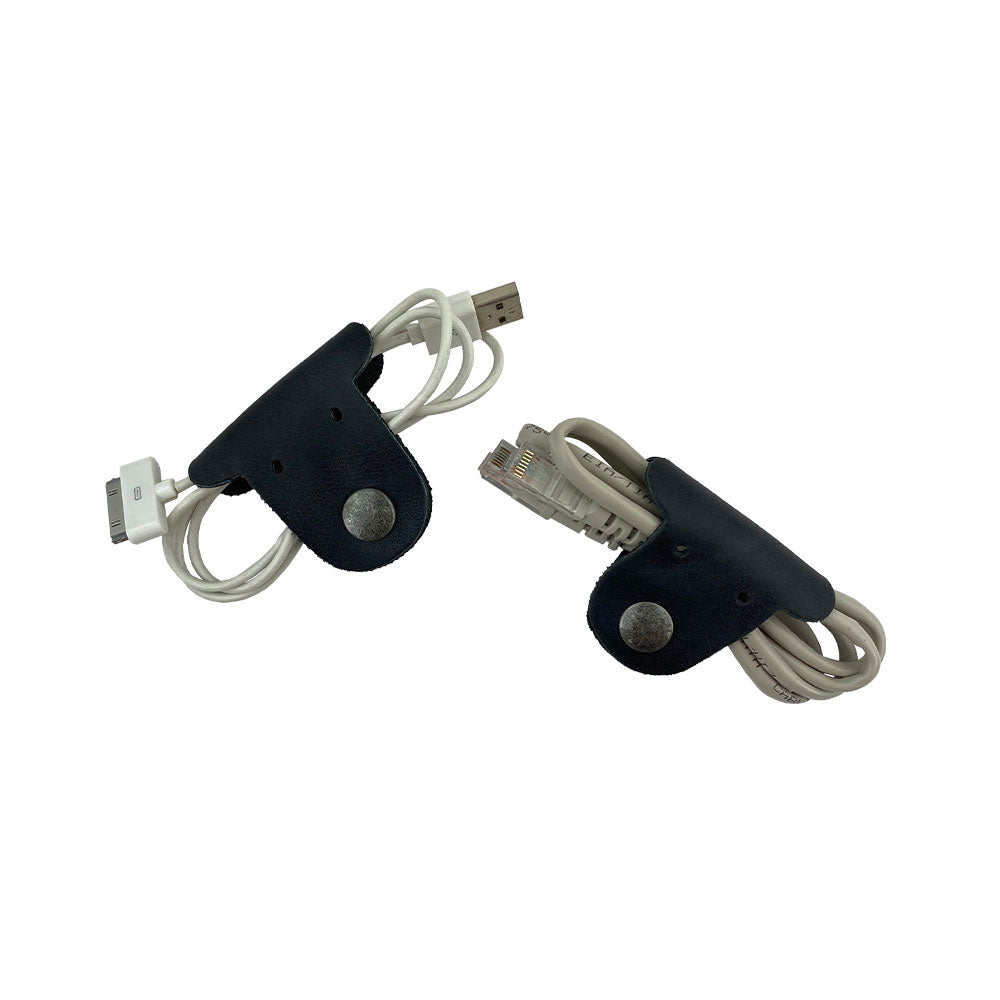 Two black Dog Shaped Cord Keepers neatly managing USB cables, a clever and cute product by Hide & Drink, crafted from Full Grain Leather. Dog Shaped Cord Keeper (Cord Clam) 2-Pack, Full Grain Leather, StockyardX, Small Batch Production, Hand Cut, Hand Sewn, Fire Branded, Artisan, Handmade in La Antigua Guatemala & Oaxaca Mexico.