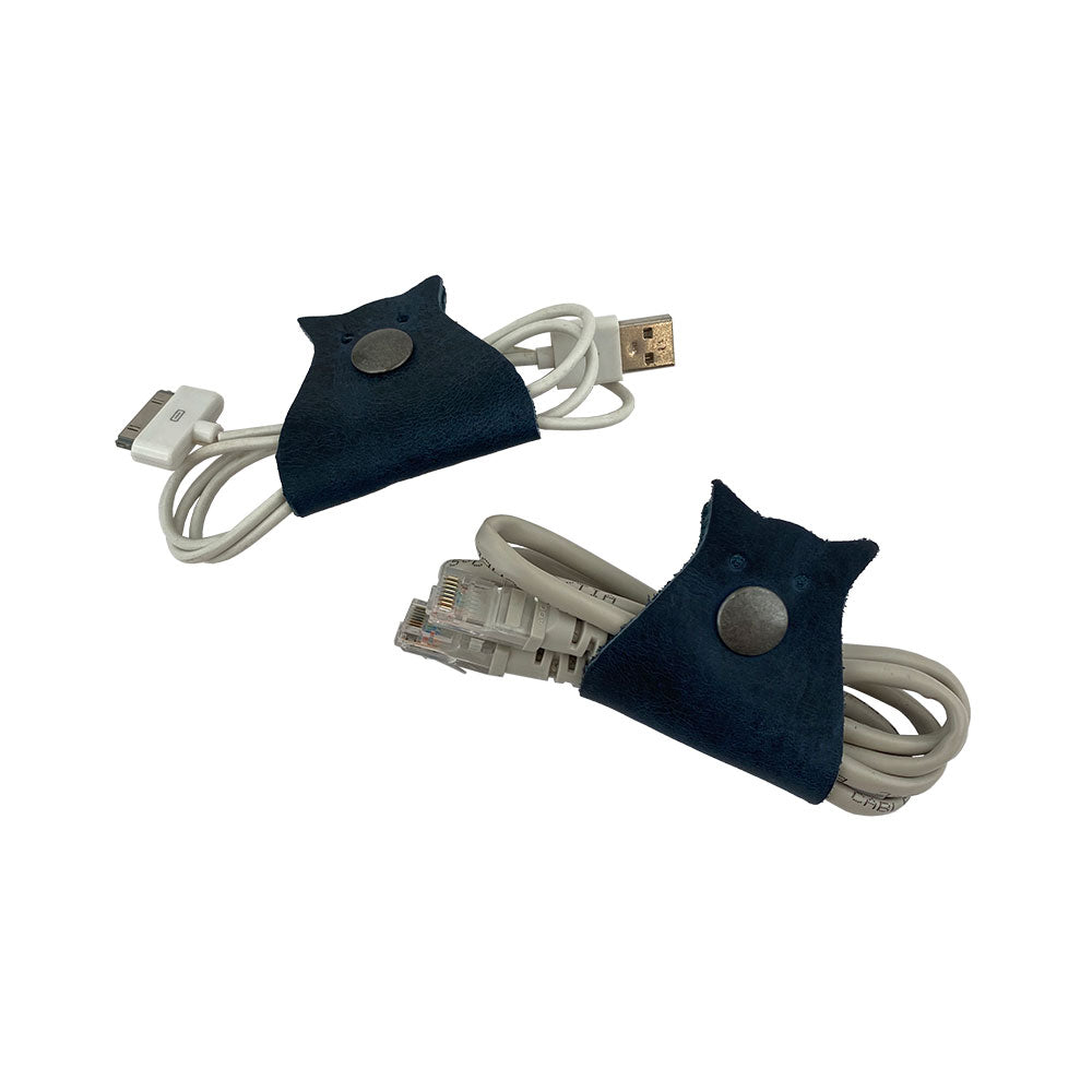 Owl Shaped Cord Keeper (2-Pack) by Hide & Drink displayed with earphones, highlighting its quality design and ease of use for cord management. Owl Shaped Cord Keeper (Cord Clam) 2-Pack. Full Grain Leather, StockyardX, Small Batch Production, Hand Cut, Hand Sewn, Fire Branded, Artisan, Handmade in La Antigua Guatemala & Oaxaca Mexico.
