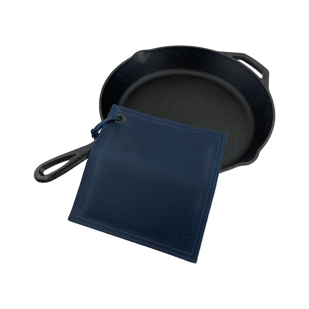 Hide & Drink Pot Pad alongside a cast iron skillet, emphasizing durability and functionality. This artisan-crafted hot pot pad is made from full grain leather.
