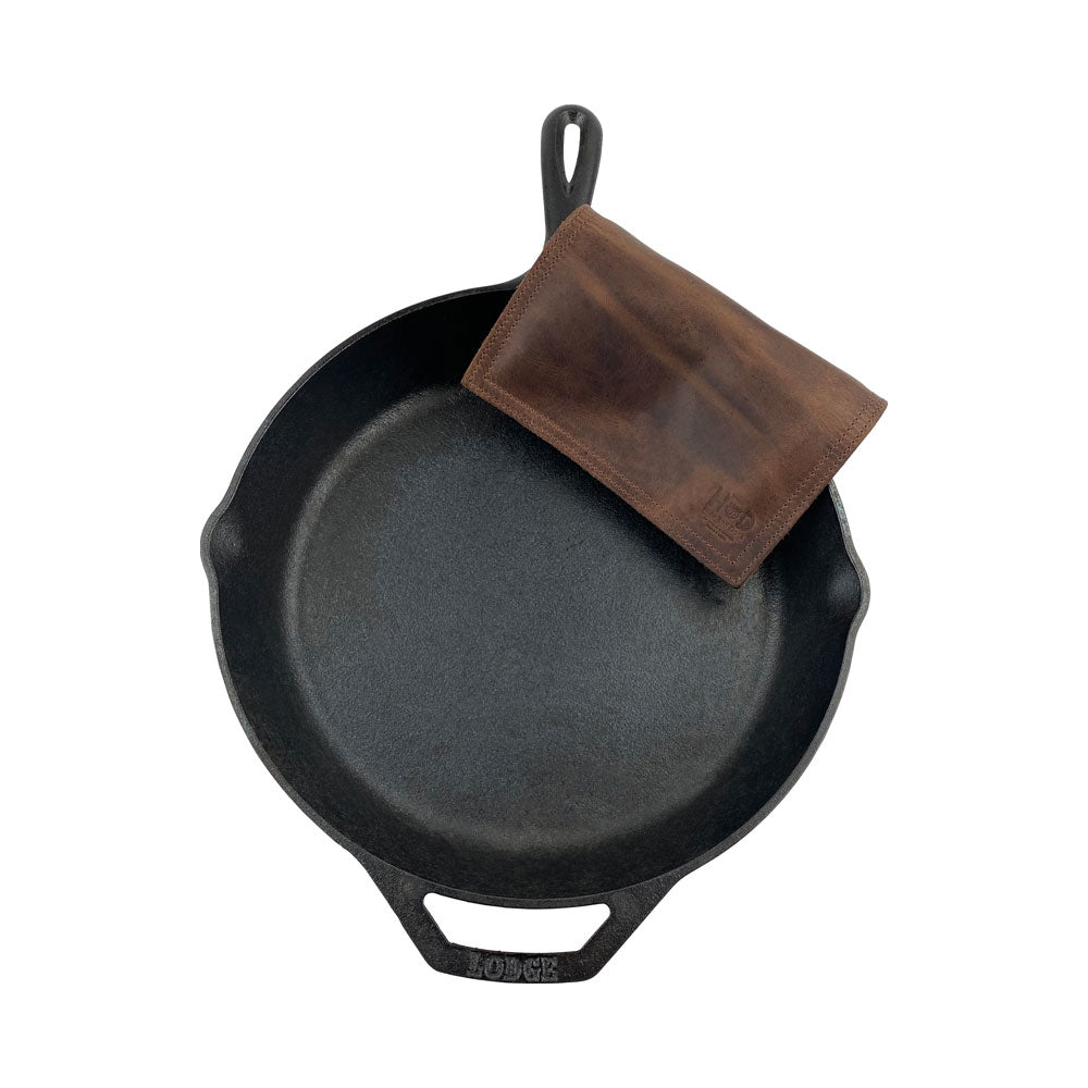 Hide & Drink Pot Pad placed next to a cast iron pot, illustrating its practicality. This rustic potholder is crafted from full grain leather with a double-layered design.