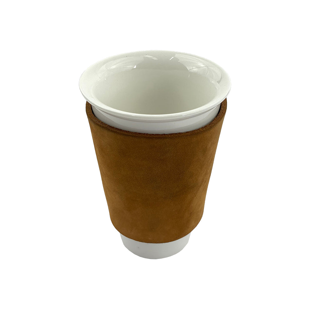 The brown leather Pint Sleeve from Hide & Drink wraps around a coffee cup, exemplifying its stylish practicality. This durable artisan piece provides temperature control and features brass metal rivets, handcrafted in La Antigua Guatemala & Oaxaca Mexico.