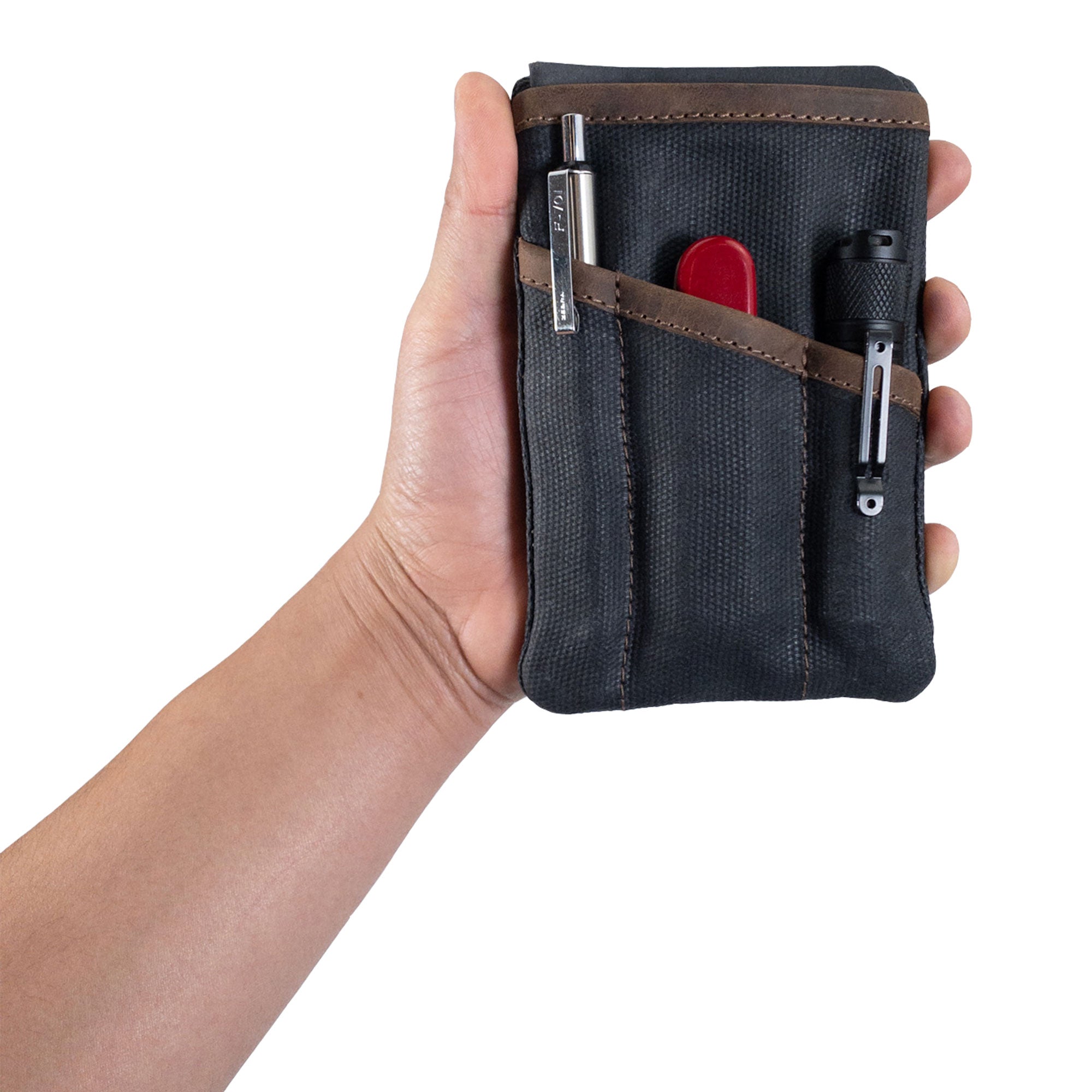 Person holding the red Multi-tool Pocket Pouch by Hide & Drink, emphasizing its ergonomic design for practicality.
