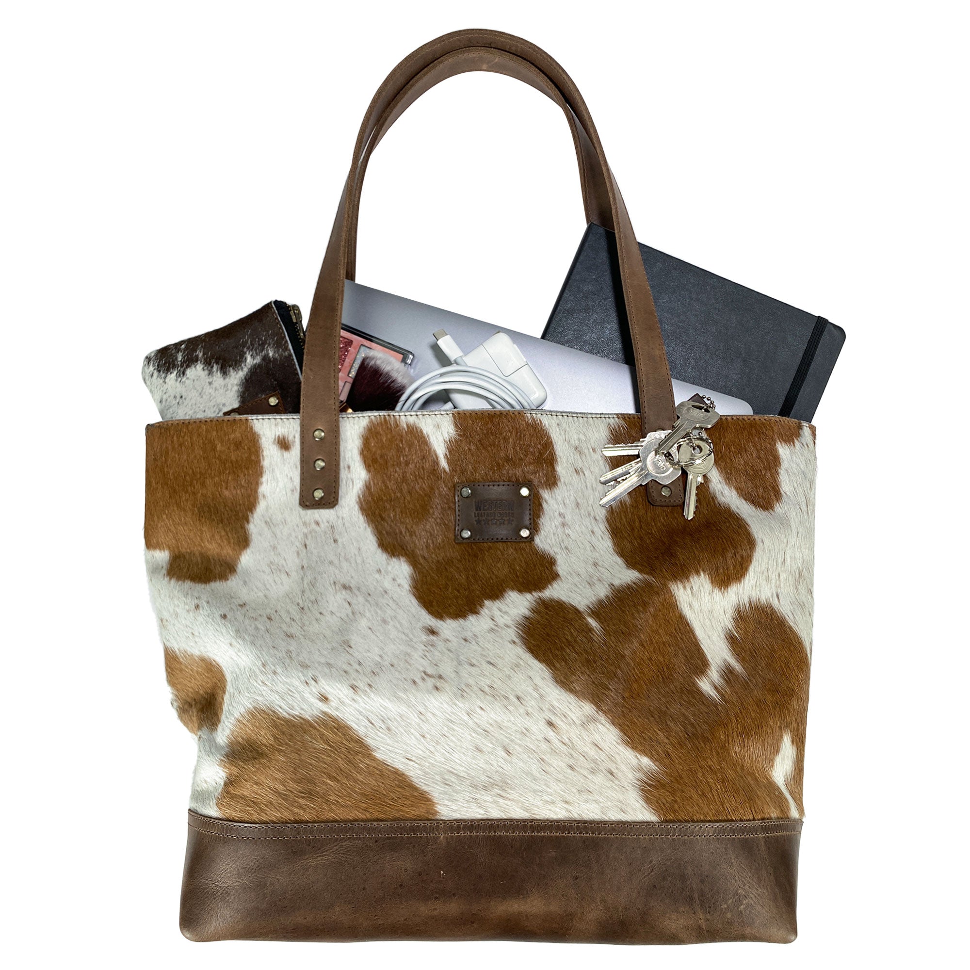 Western Leather Works Formal Tote Bag in use, displaying its spacious capacity with essentials like a laptop and notebook. Made from Hair on Hide Full Grain Leather, this tote combines practicality with cowboy style. Hand cut and hand sewn, featuring a plaid cotton interior lining. Artisan, handmade in La Antigua Guatemala & Oaxaca Mexico.