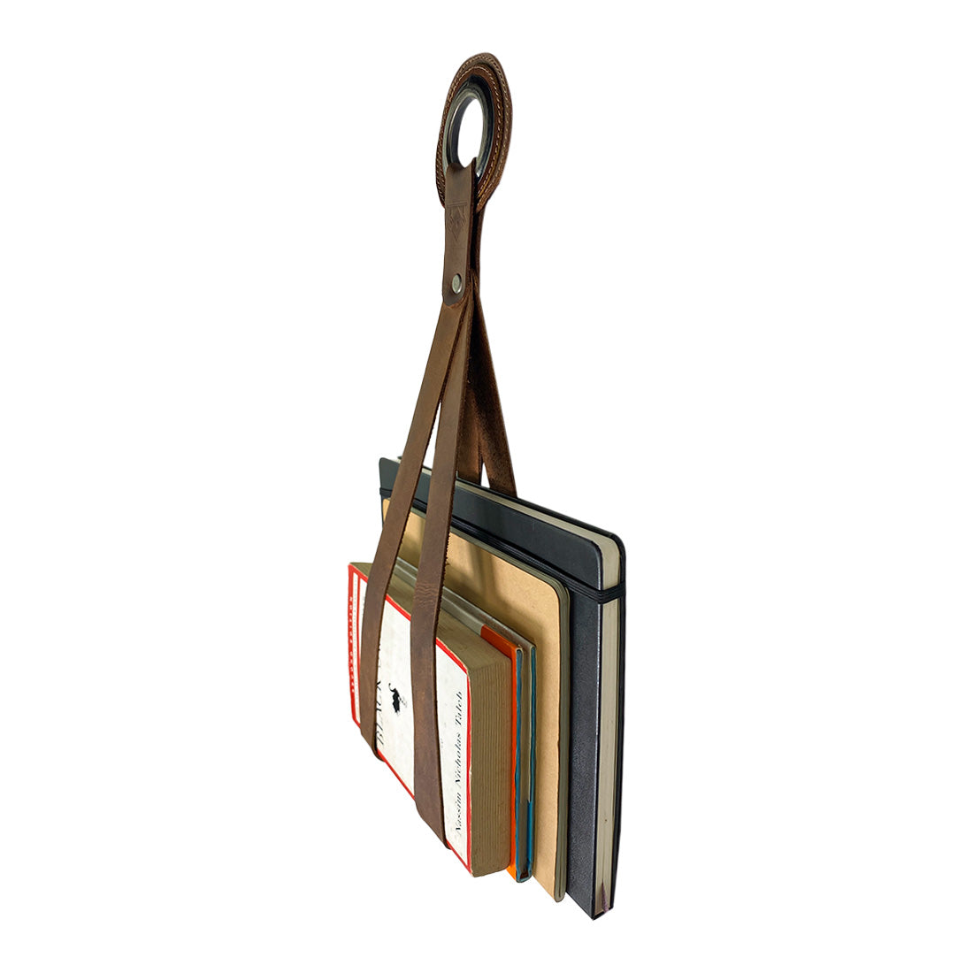 The Book Wall Hanger by Leather At Home, elegantly holding multiple notebooks. This rustic wall organizer for book lovers is artisan-crafted from full grain leather, combining practicality and aesthetics in one. Handmade in La Antigua Guatemala & Oaxaca Mexico, it features unique qualities from small batch production.