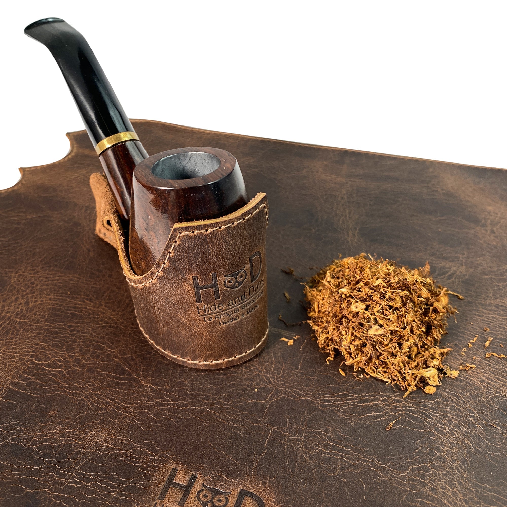 Tobacco Pipe Holder by Hide & Drink displayed next to loose tobacco, illustrating its practical use and elegant design. This Tobacco Pipe Holder (Pipe not Included) provides a portable & adjustable stand, perfect for the smoking enthusiast. Made of durable full grain leather, it showcases small batch production with careful hand cutting and stitching by artisans in La Antigua Guatemala & Oaxaca Mexico.