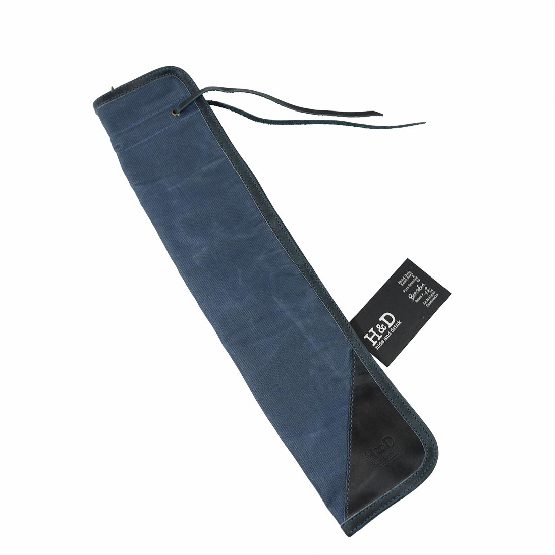 Side view of the blue Hide & Drink Drummstick Bag with an informational tag, showcasing its unique design. The Waxed Canvas & Full Grain Leather construction makes this Drumstick Bag Holder a must-have for drummers, emphasizing the handmade quality from artisans in La Antigua Guatemala & Oaxaca Mexico.