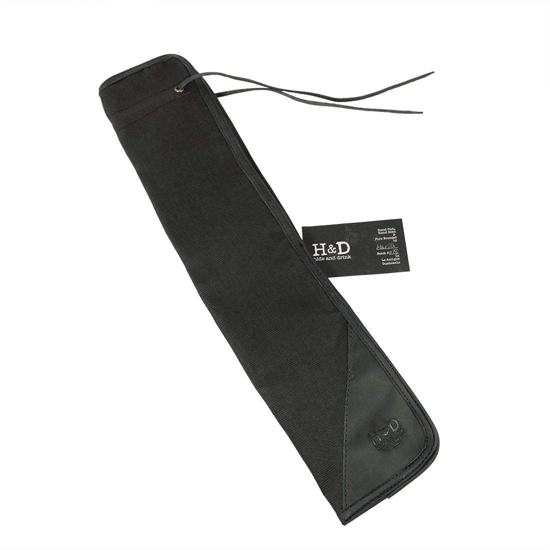 The black Hide & Drink Drummstick Bag displayed with an informational tag, highlighting its premium materials of Waxed Canvas & Full Grain Leather. This practical Drumstick Bag Holder is a top choice for musicians, exemplifying hand crafted excellence from small batch production in La Antigua Guatemala & Oaxaca Mexico.
