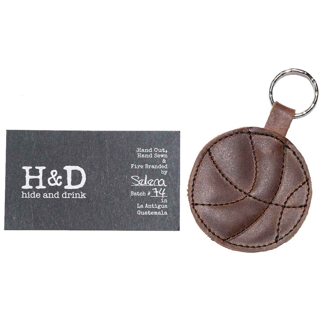 The Basketball Keychain by Hide & Drink alongside a branded tag, showcasing the artisan craftsmanship. This unique key ring is designed for sports fans and makes an excellent gift for players, highlighting the brand’s commitment to small batch production.