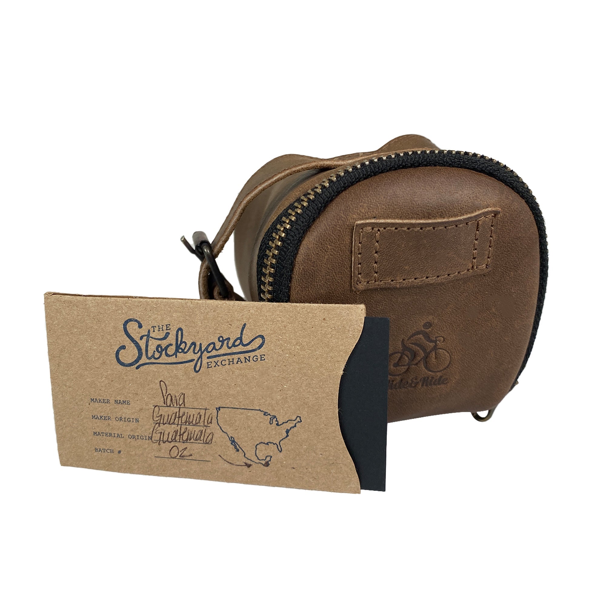 Hide & Ride Under Seat Pouch displayed alongside a special card showcasing its artisan craftsmanship and production details. This Bicycle Under Seat Pouch exemplifies the blend of style and utility, making it a key accessory bag for bikers. Handcrafted from full grain leather, it emphasizes small batch production in La Antigua Guatemala & Oaxaca Mexico.