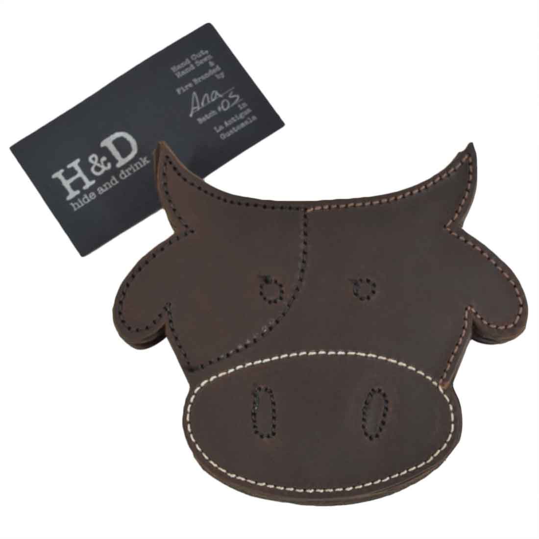 One Milk Cow Coaster from the Milk Cow Coaster Set (6-Pack) by Hide & Drink, displayed with the company's branding tag, showcasing its artisan quality and handmade characteristics. A delightful addition for any kitchen or coffee table. Durable Thick Leather Milk Cow/Animal Farm Cute Shaped Coasters (6-Pack) Full Grain Leather, StockyardX, Small Batch Production, Hand Cut, Hand Sewn, Fire Branded, Artisan, Handmade in La Antigua Guatemala & Oaxaca Mexico.
