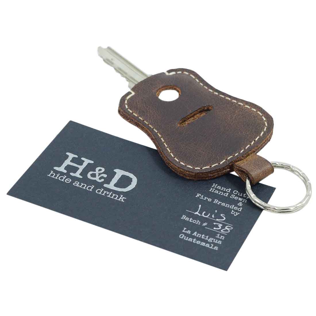 Guitar Keychain by Hide & Drink displayed with branding card, featuring its artisan craftsmanship. This keyring, made from Full Grain Leather, is perfect for a convenient key holder and emphasizes the quality of handmade goods from La Antigua Guatemala & Oaxaca Mexico.