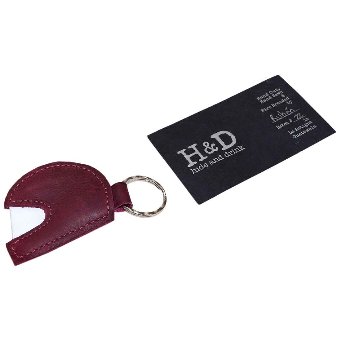 The Hide & Drink Motorcycle Helmet Keychain alongside its branding card, displaying its handmade quality and authenticity. This charming key ring, made from full grain leather, is a stylish accessory for any biker, emphasizing small batch production.