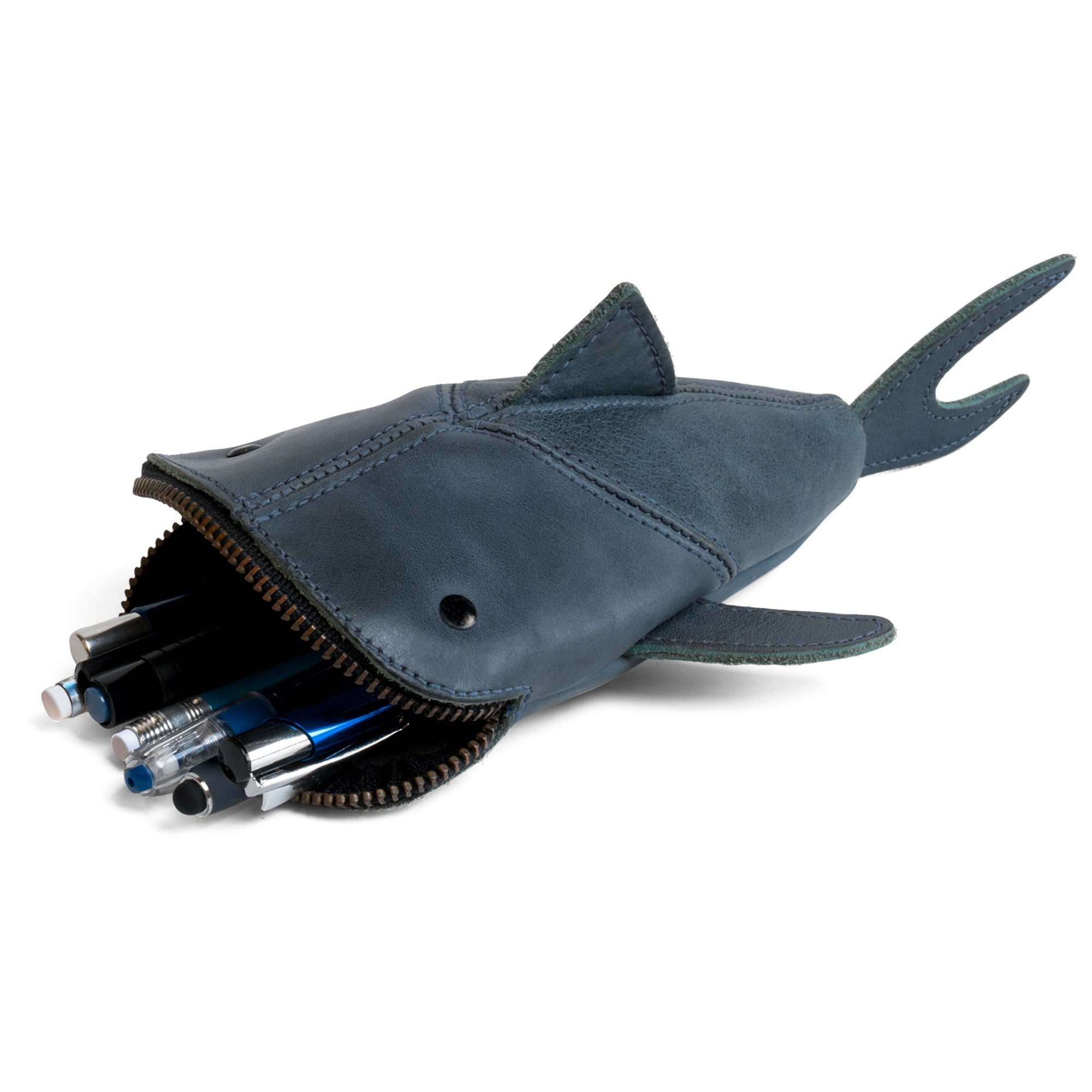 Blue variant of the Leather Shark Pouch from Hide & Drink, filled with pens and art supplies. This zippered case combines utility with style, serving as a pencil purse or zippered coin pouch. Made from full grain leather, this playful shark shaped case showcases small batch artisan production from La Antigua Guatemala & Oaxaca Mexico.