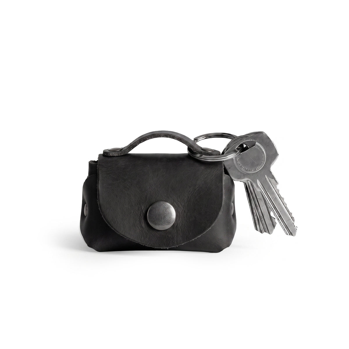 A stylish Tiny Handbag Keychain in black leather by Hide & Drink, featuring a key ring holder. This functional piece is made from high-quality Full Grain Leather and emphasizes small batch production and meticulous artisan craftsmanship.