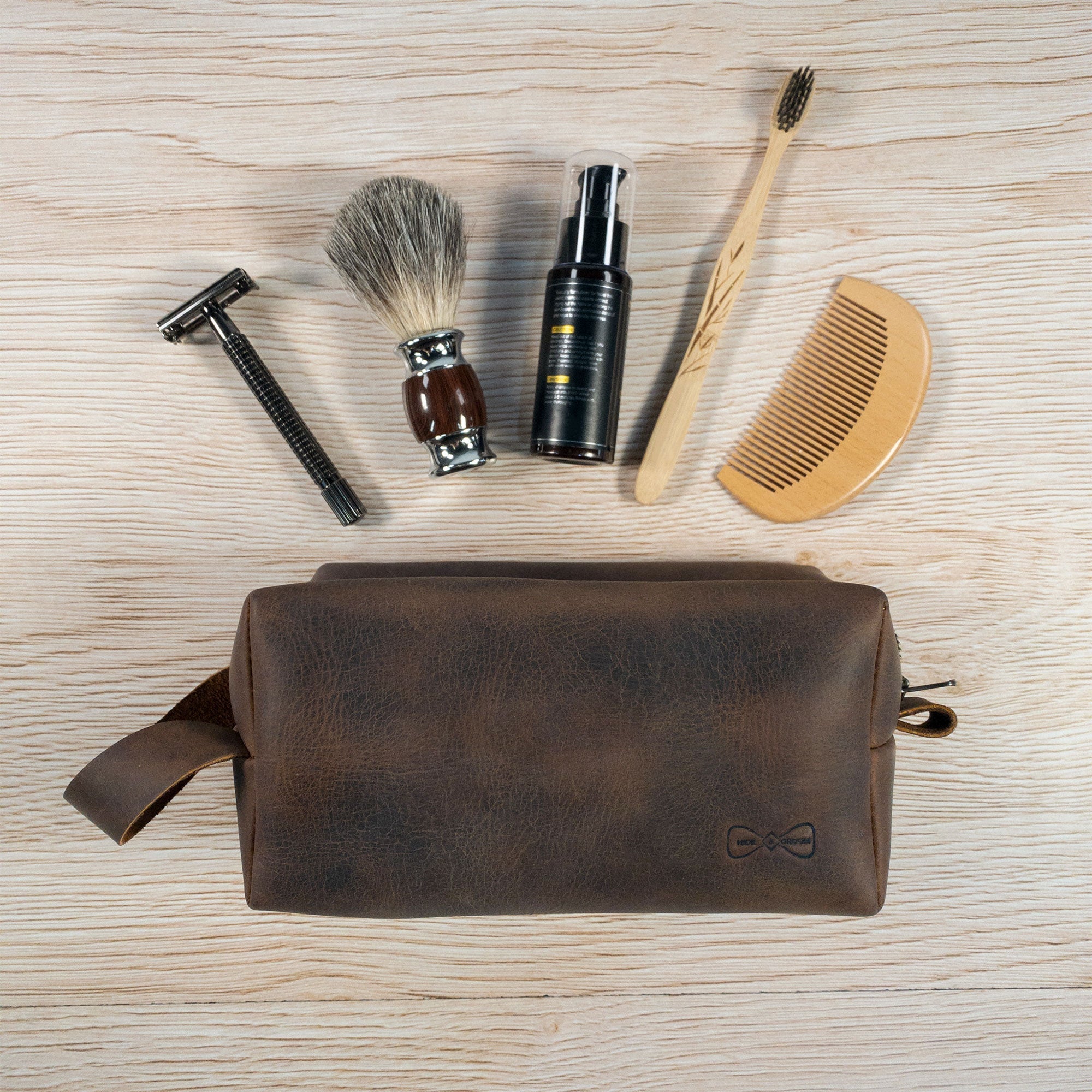 An aerial view of Hide & Groom's toiletry bag for groomsmen, surrounded by grooming essentials like a razor and brush. This rustic them is ideal for best men and made from quality full grain leather, featuring small batch artisanal production for a refined shaving kit storage solution.
