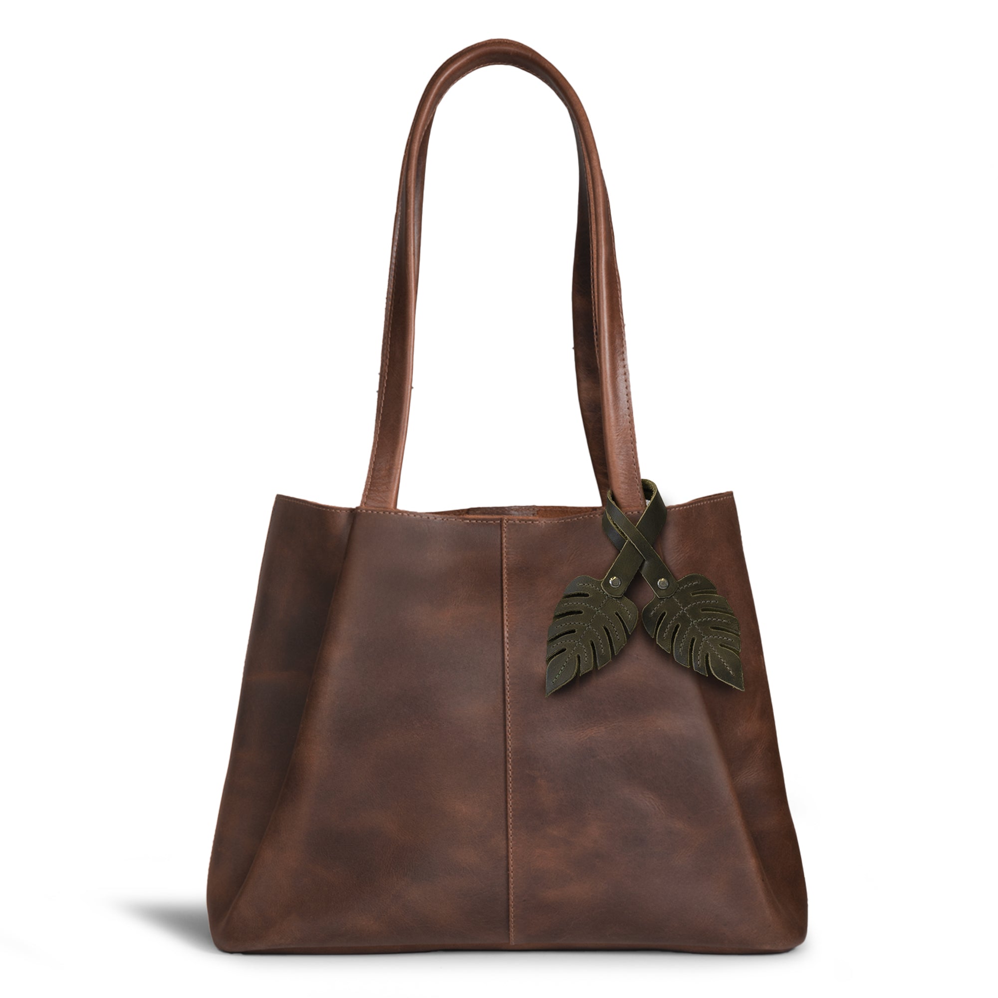 Hide & Drink Bag Charms attached to a stylish brown handbag, showcasing a bird design perfect for personalization. This accessory serves as a purse charm for tote & backpacks made from durable full grain leather, demonstrating StockyardX's commitment to small batch production. Each piece highlights hand cut, hand sewn artistry and fire branding, handmade in La Antigua Guatemala & Oaxaca Mexico.